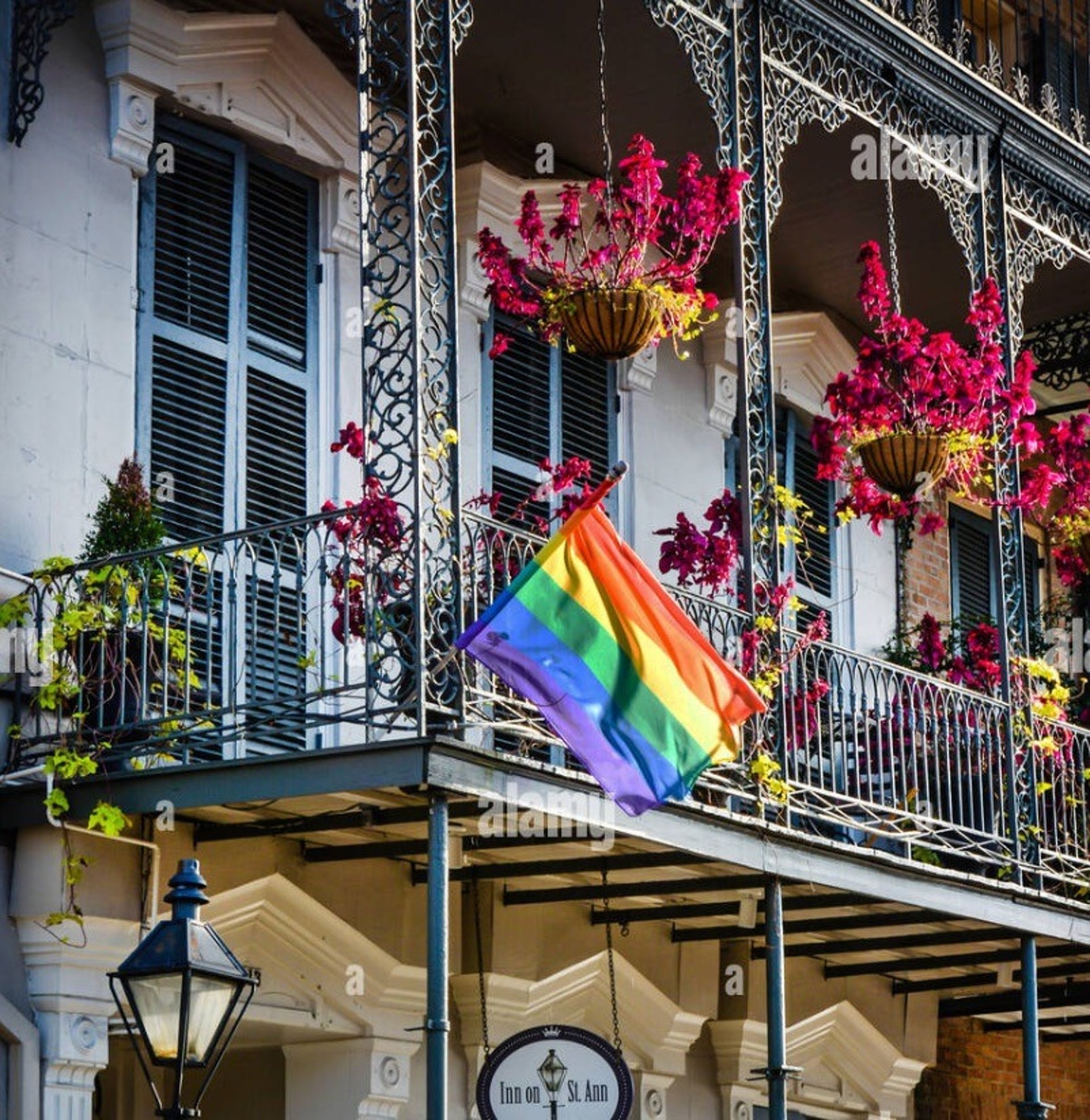A street sign on a pole in front of a rainbow flag