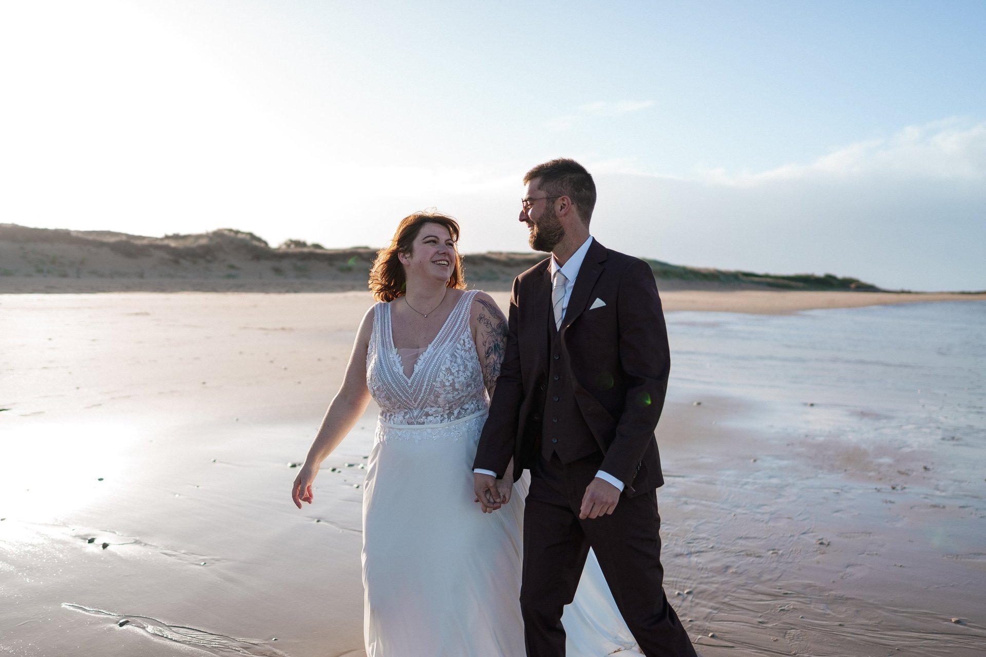 Les mariés, rayonnants de bonheur, se promènent main dans la main sur une plage ensoleillée le jour de leur mariage.