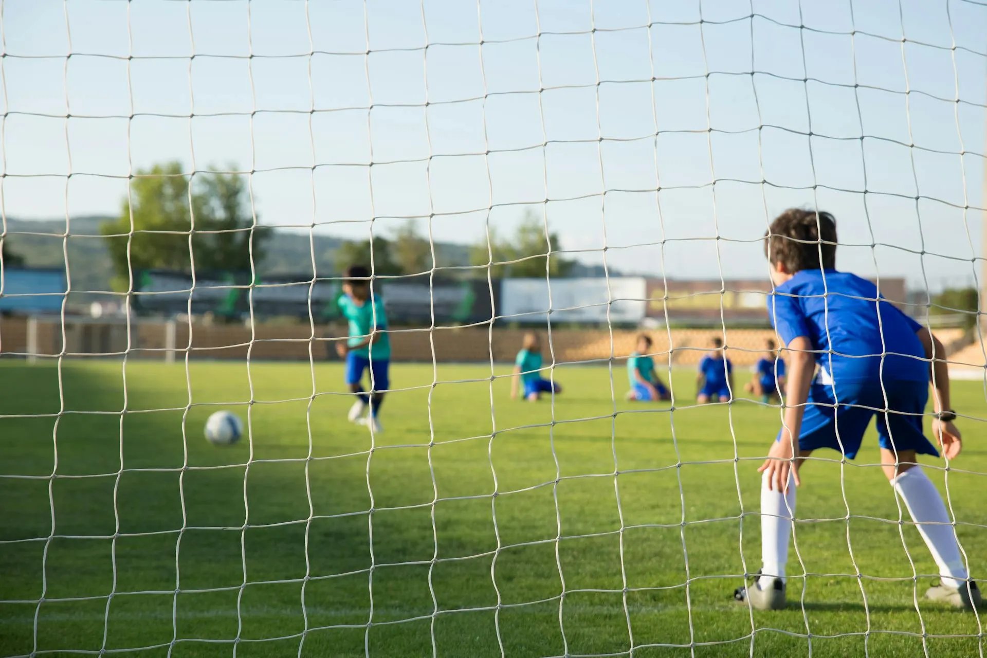 children playing soccer on a green grass pitch in front of a goal