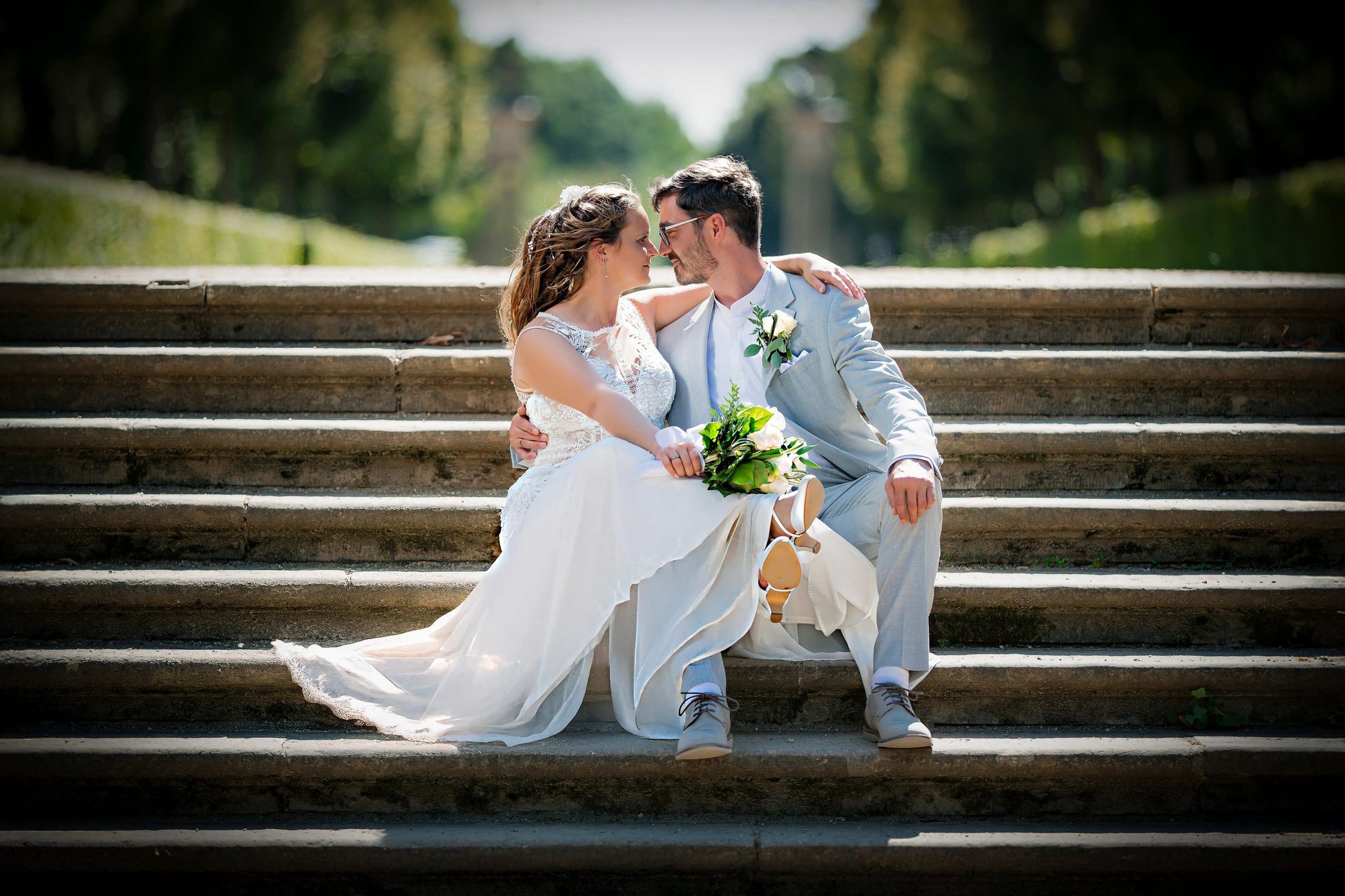 Romantisches Brautpaar sitzt auf einer Parktreppe – emotionale Hochzeitsfotografie im Freien.