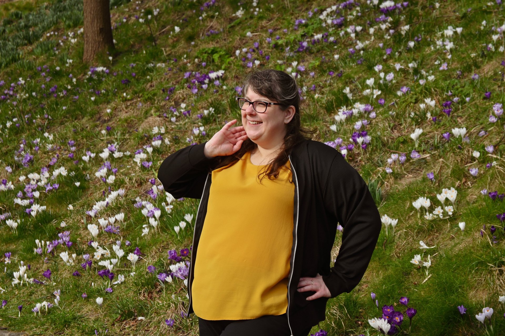 Laura is standing in front of a field of purple and white flowers, looking away from the camera with a soft smile on her face