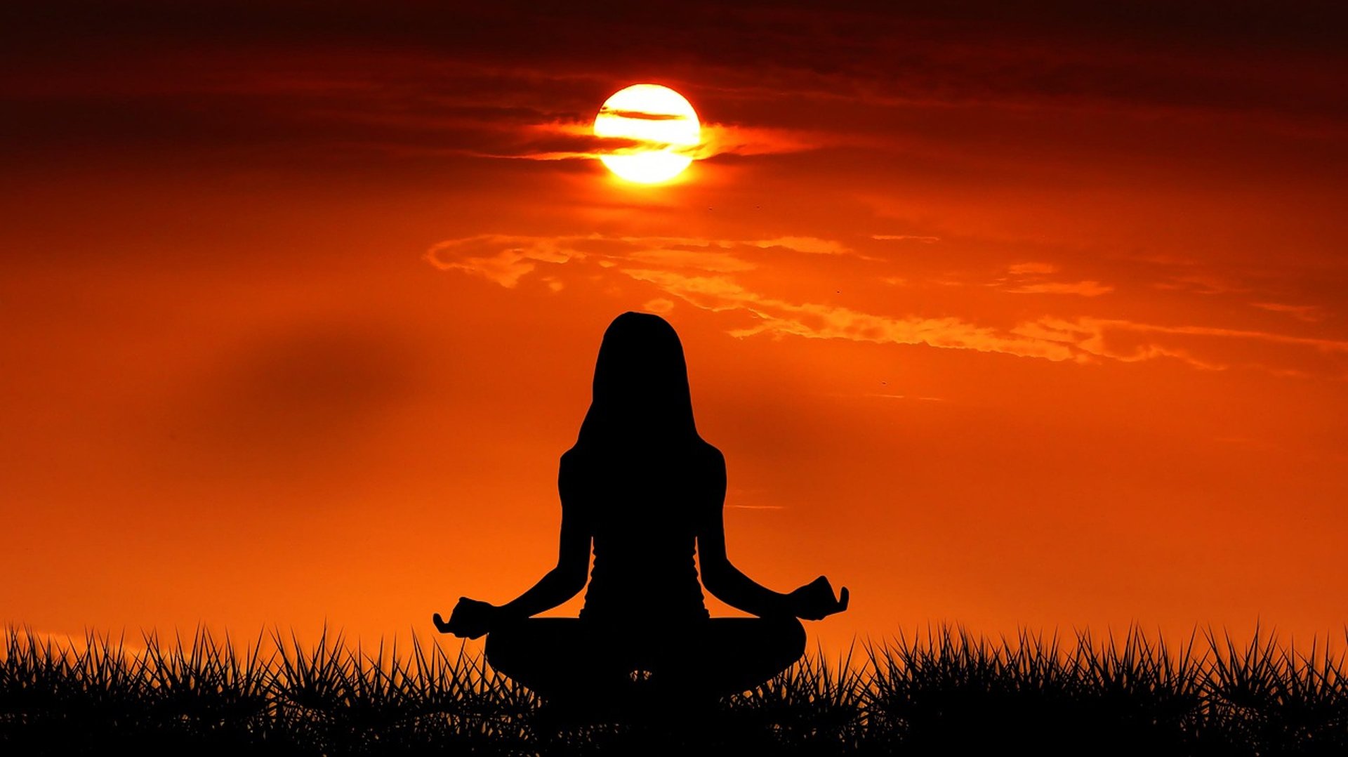 shadow form of a woman in lotus position facing a Sunrise in a deep orange sky