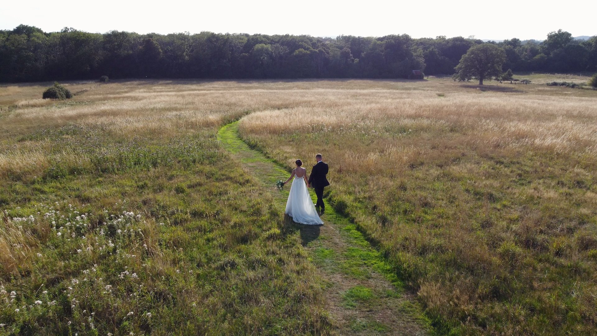 A bride and groom embracing at the end of a path, surrounded by flowers and greenery.