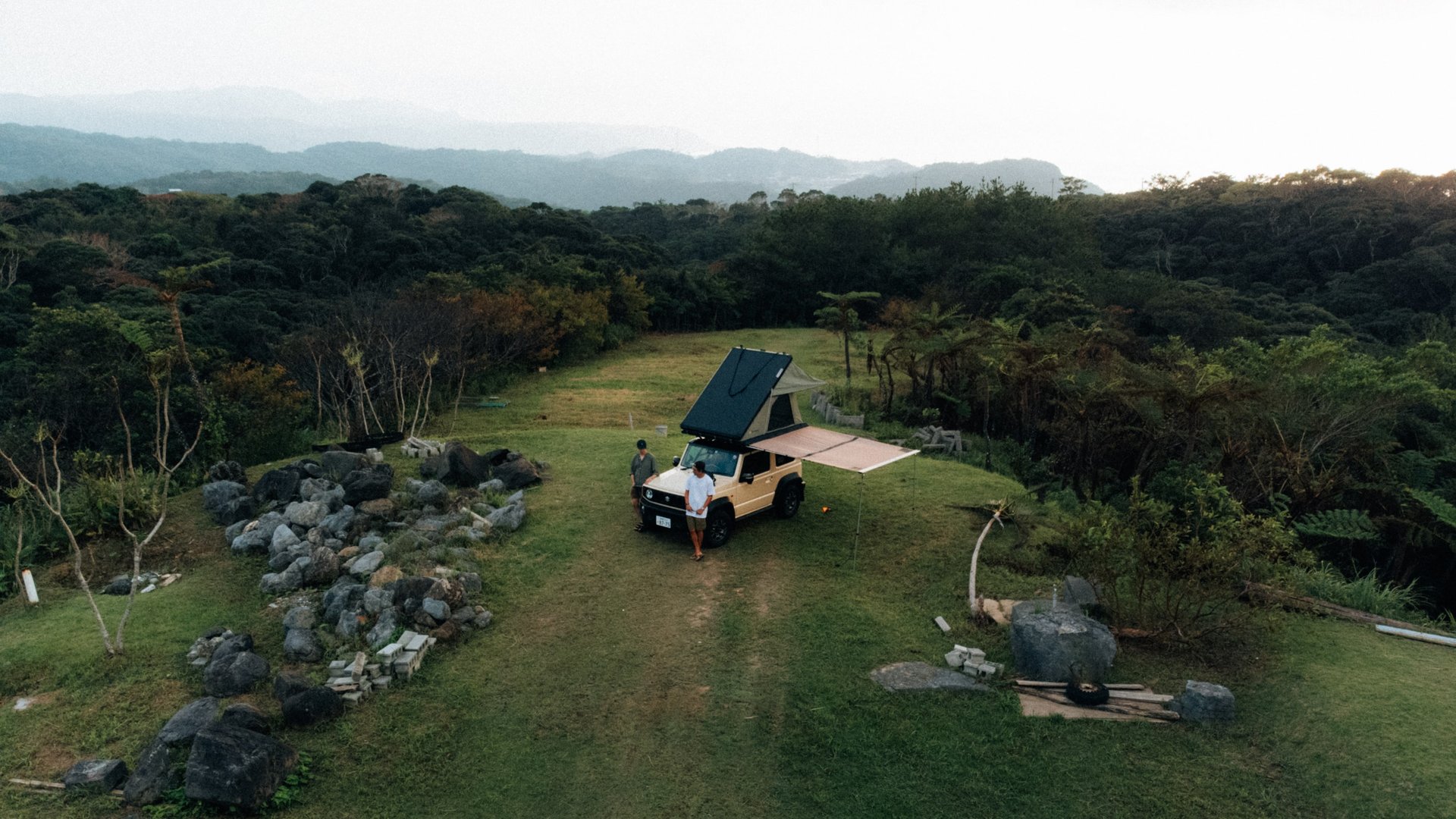 Aerial view of a Suzuki Jimny camping car set up in a grassy area with surrounding trees and rocks in Okinawa | Evertrail Oki