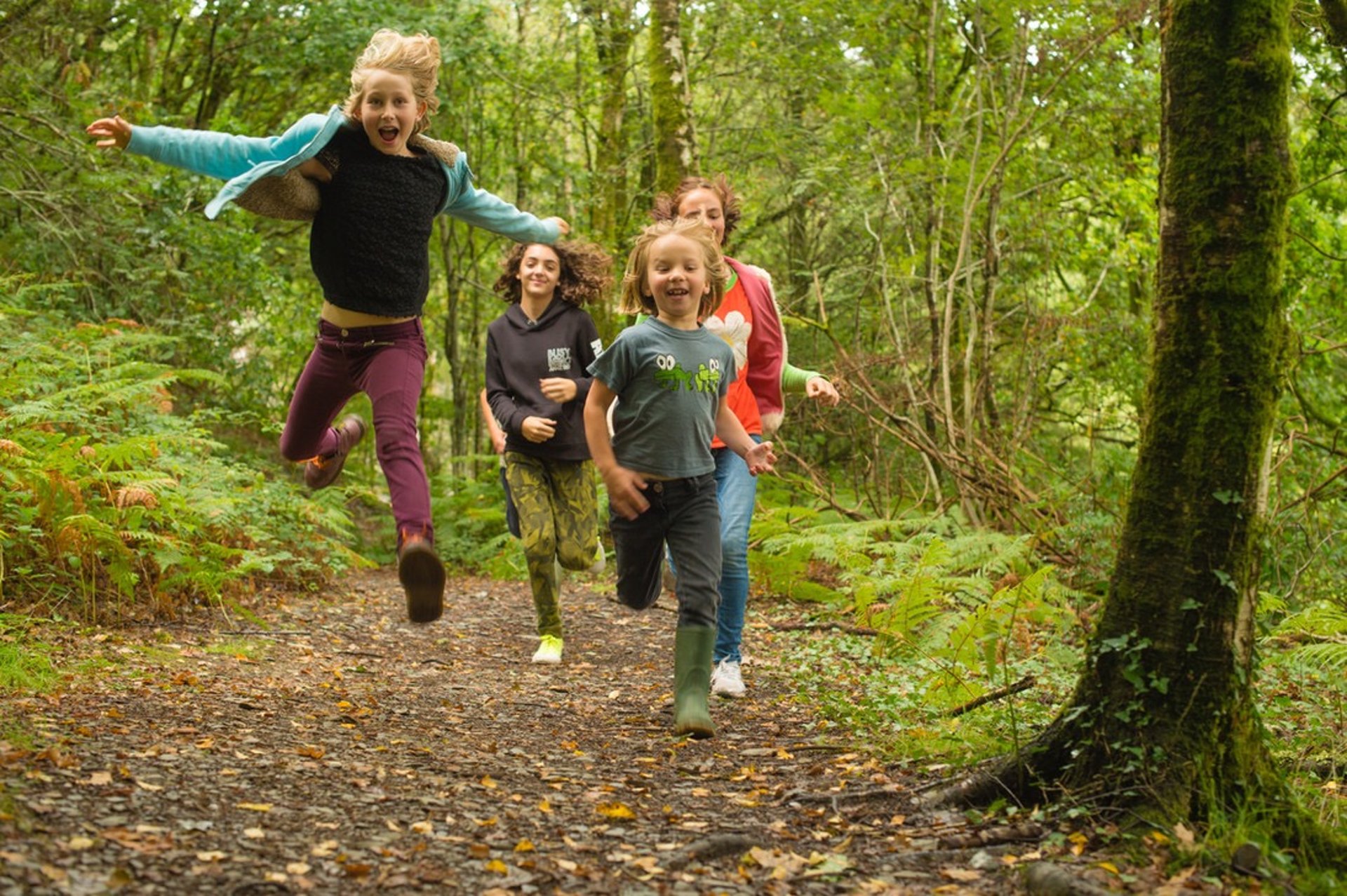 A family running along a forest trail with a child leaping in the air