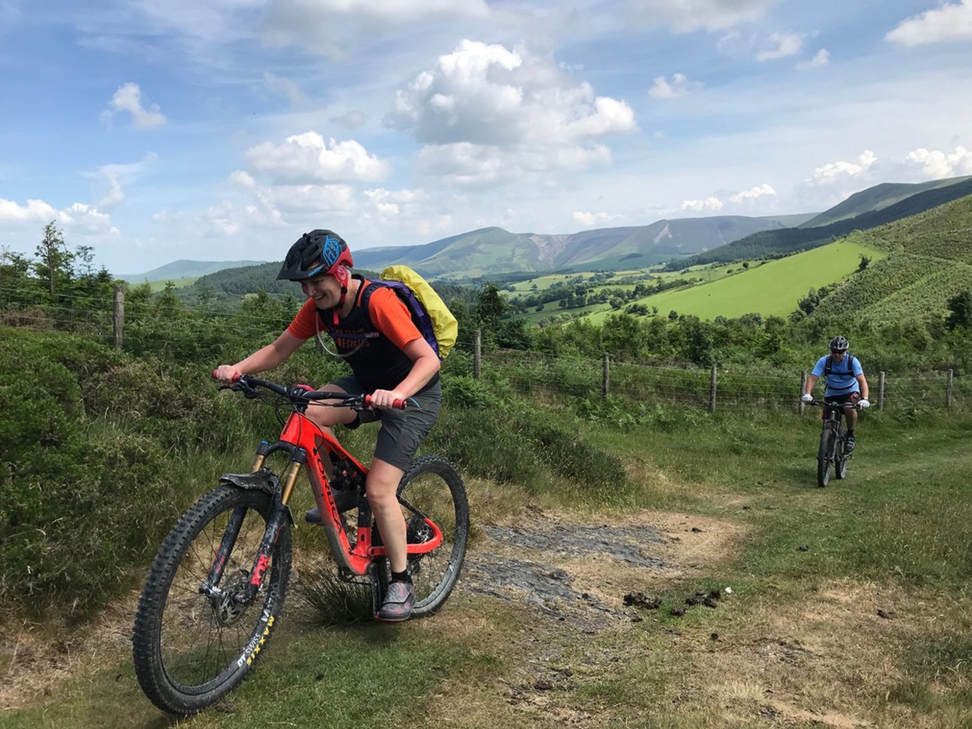 Two mountain bikers cycling up a track with hills in the background