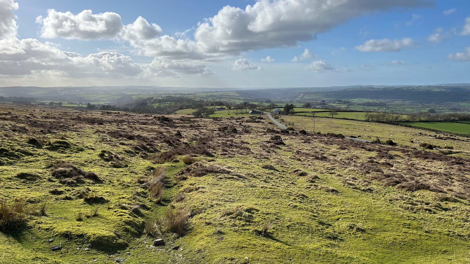The rough terrain of the moorland with distant hill behind and clouds above in a blue sky