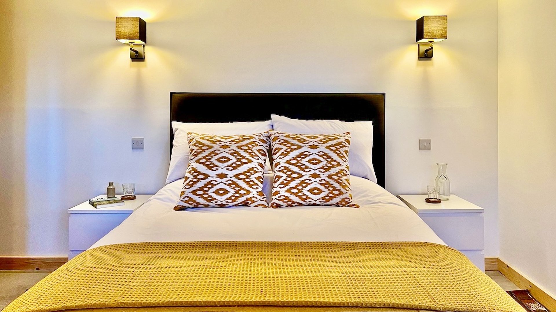 a large bed with wall lights and colourful cushions and throw