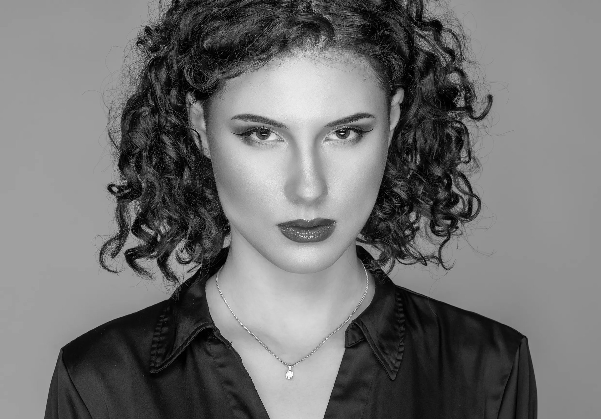 Porträt einer jungen Frau mit lockigem Haar und elegantem Ausdruck, fotografiert im Studio von LensAndLook.