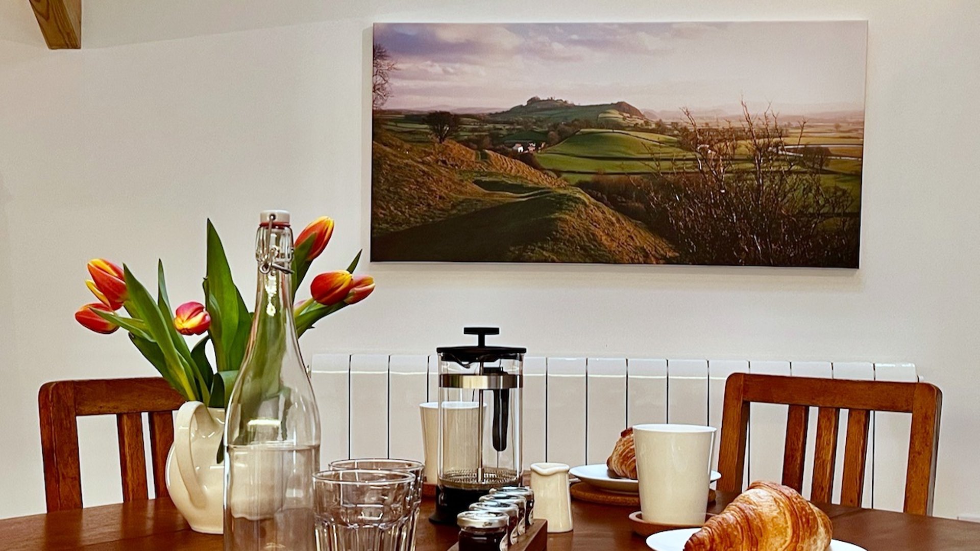 a table and chairs with crockery and glasses and picture behind