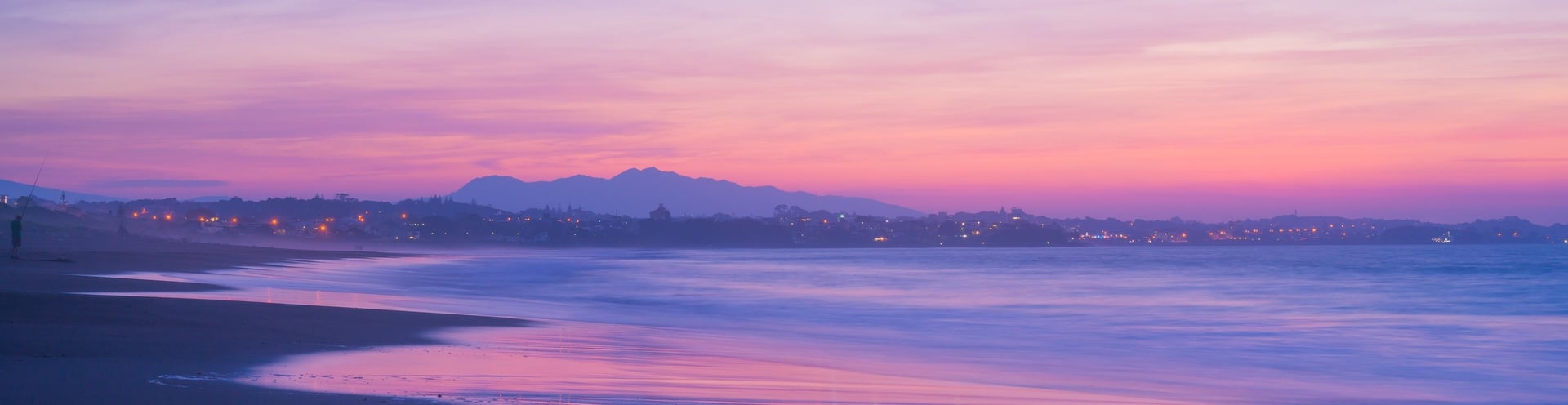man stands on end of dike watching setting sun over sea