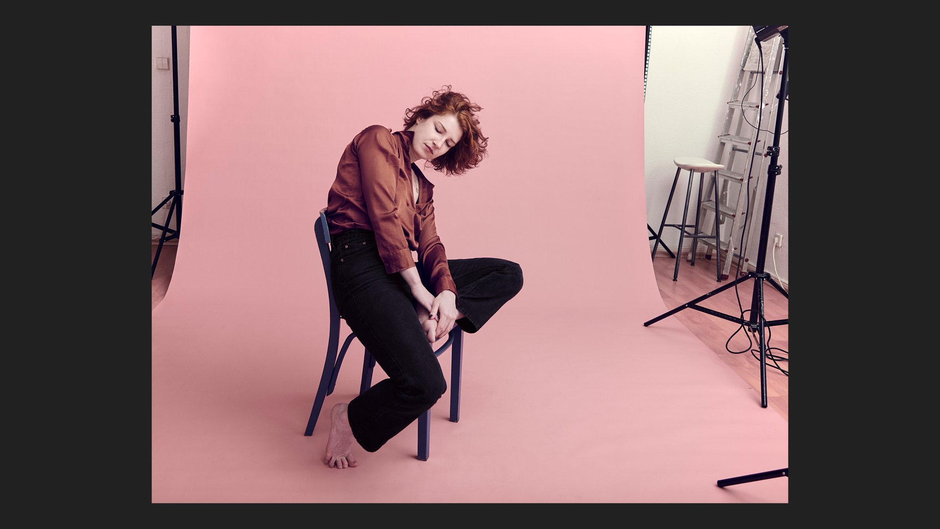 Eine junge Frau sitzt auf einem blauen Stuhl in einem Fotostudio.
