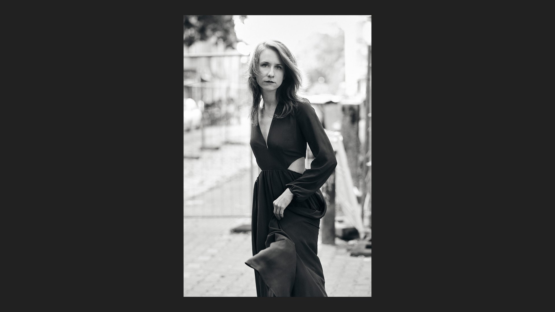 A young woman wearing a dress standing in the street.