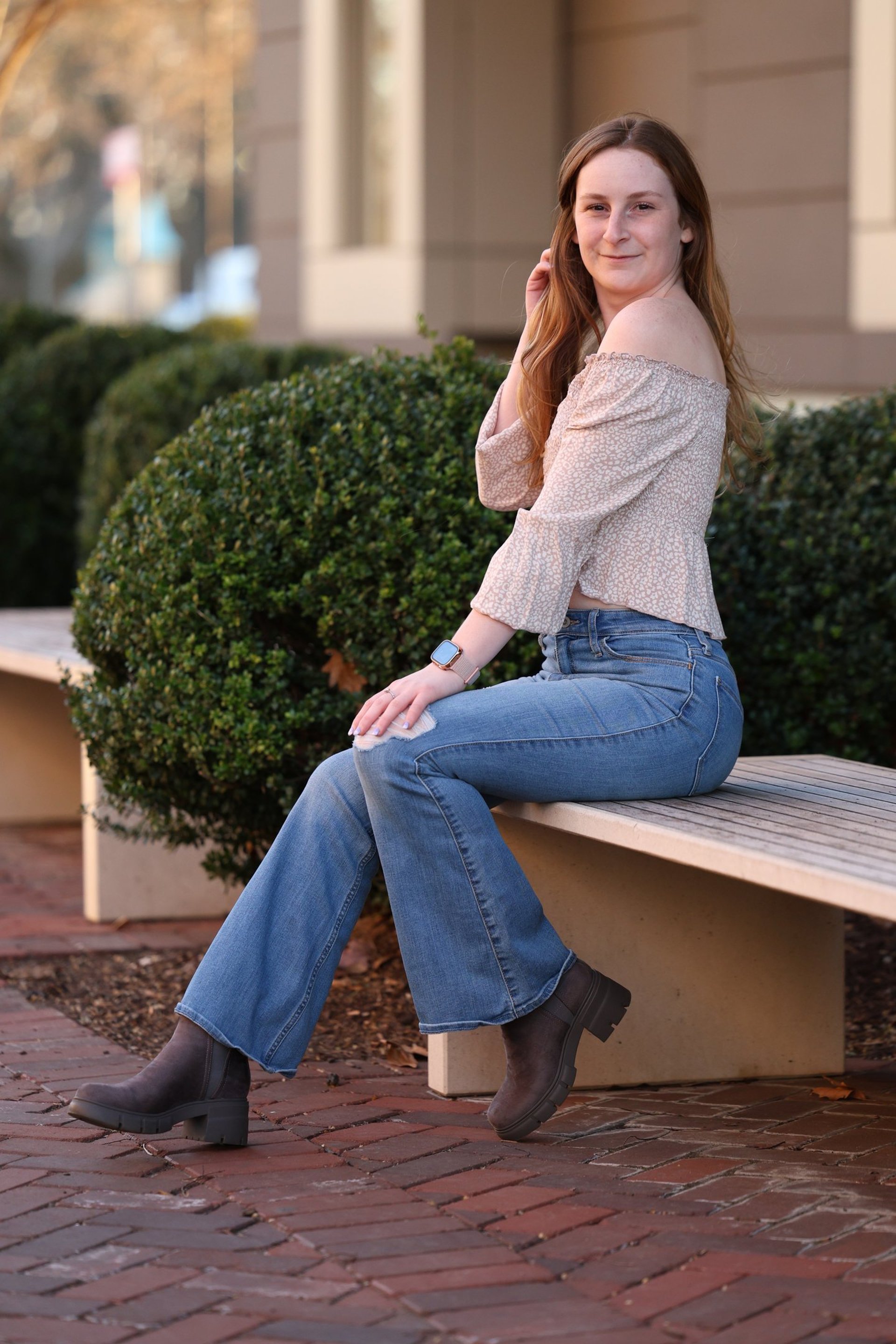 woman in black long sleeve shirt and blue denim jeans sitting on white concrete wall