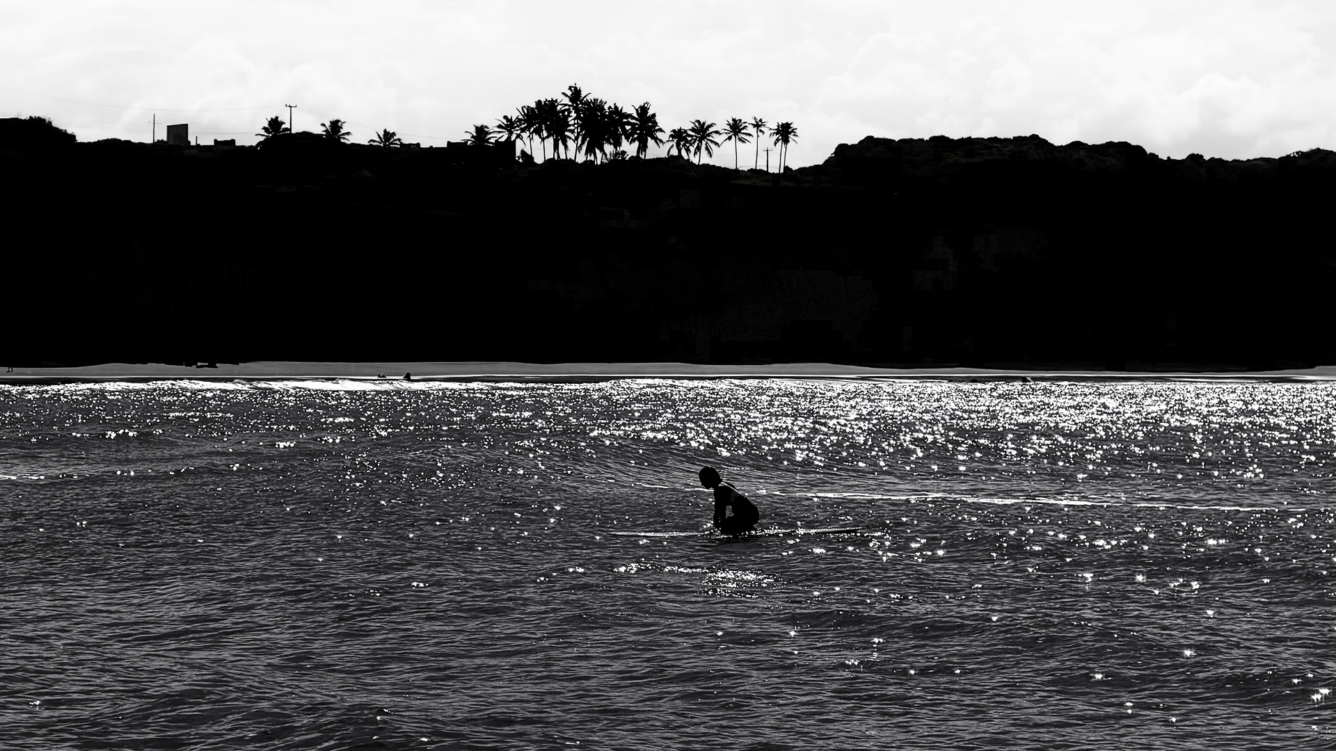 a lone surfboarder is silhouetted against a colorful sunset