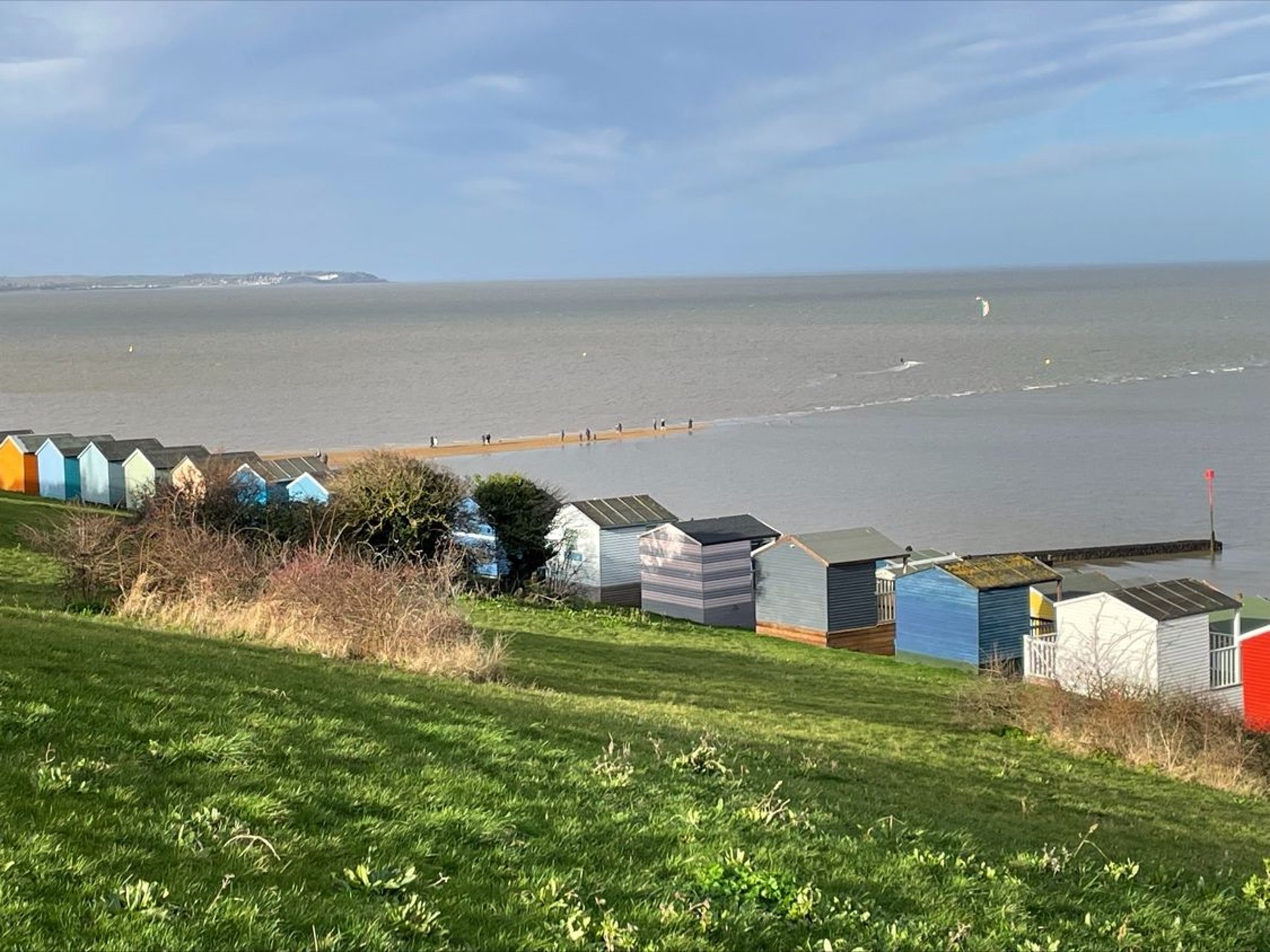 a row of rbighly coloured beach huts in Tankerton with a view over the sea towards Sheppey
