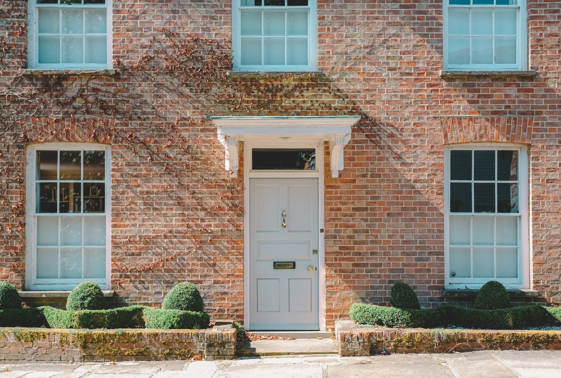 front of a brick house with white door and two windows downstairs and three windows on first floor. stone floor, low edges