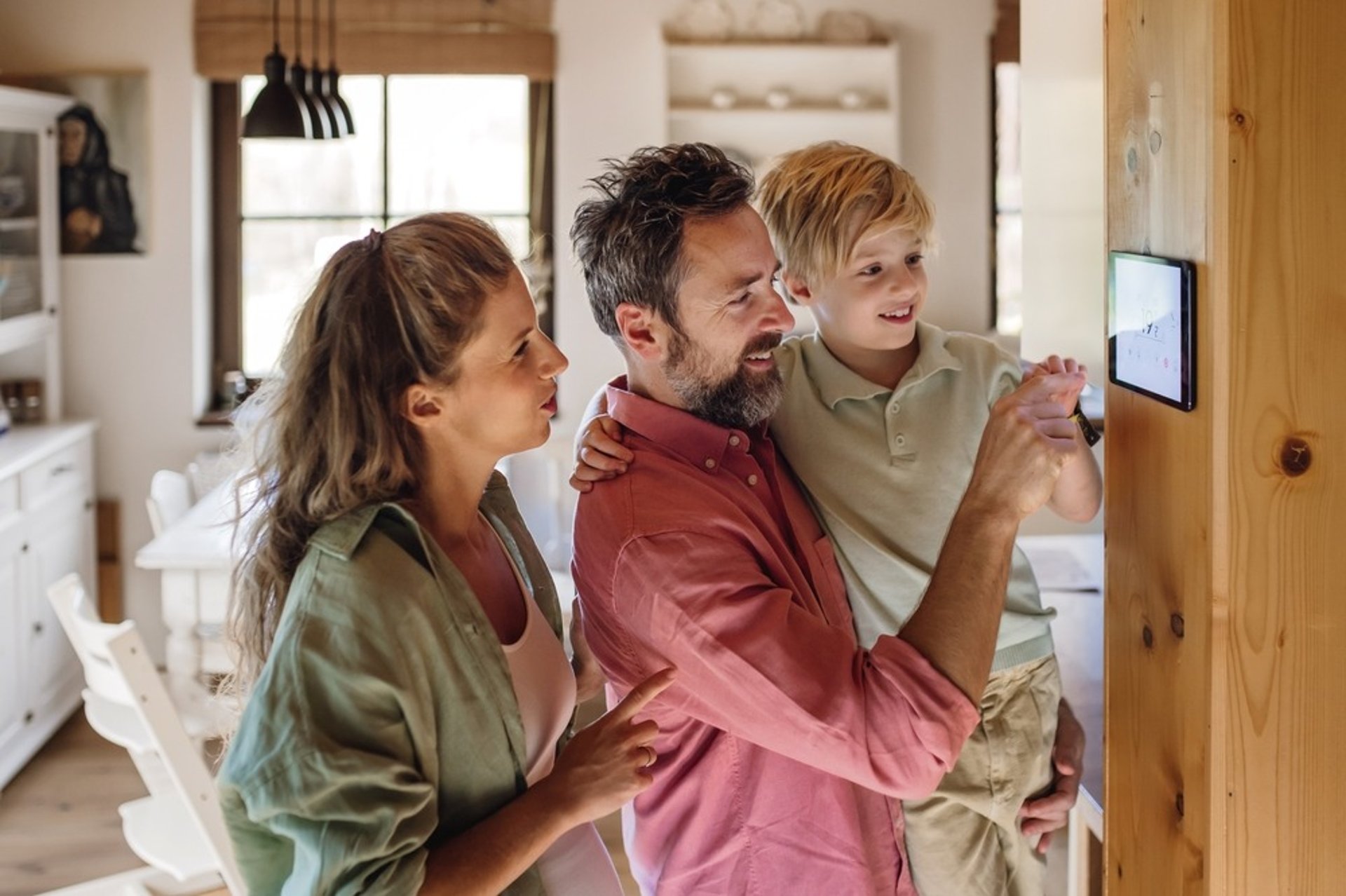 family of three smiling and looking at tablet mounted on wall