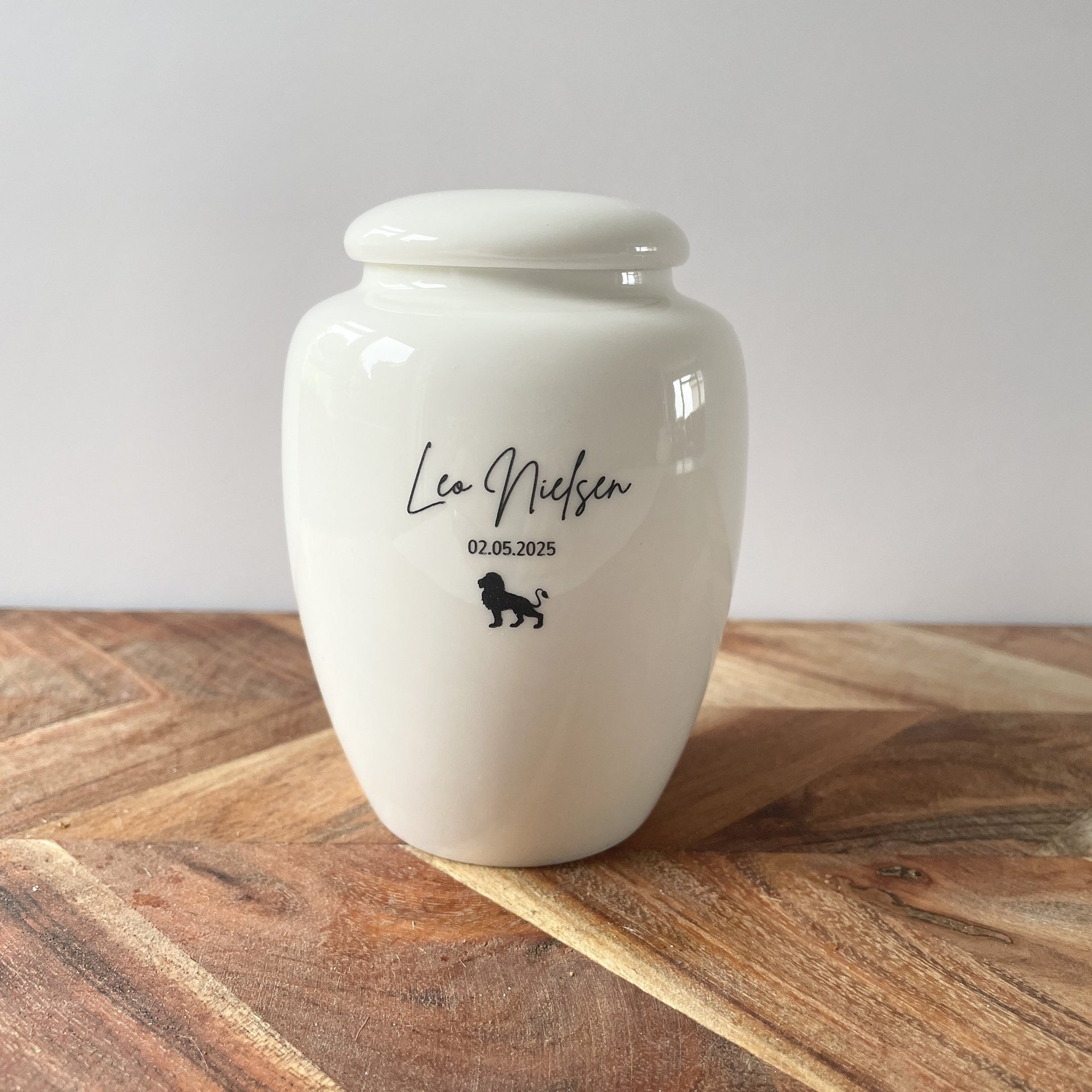 Elegant white ceramic urn with glossy finish, black script text “Leo Nielsen” and a small lion icon