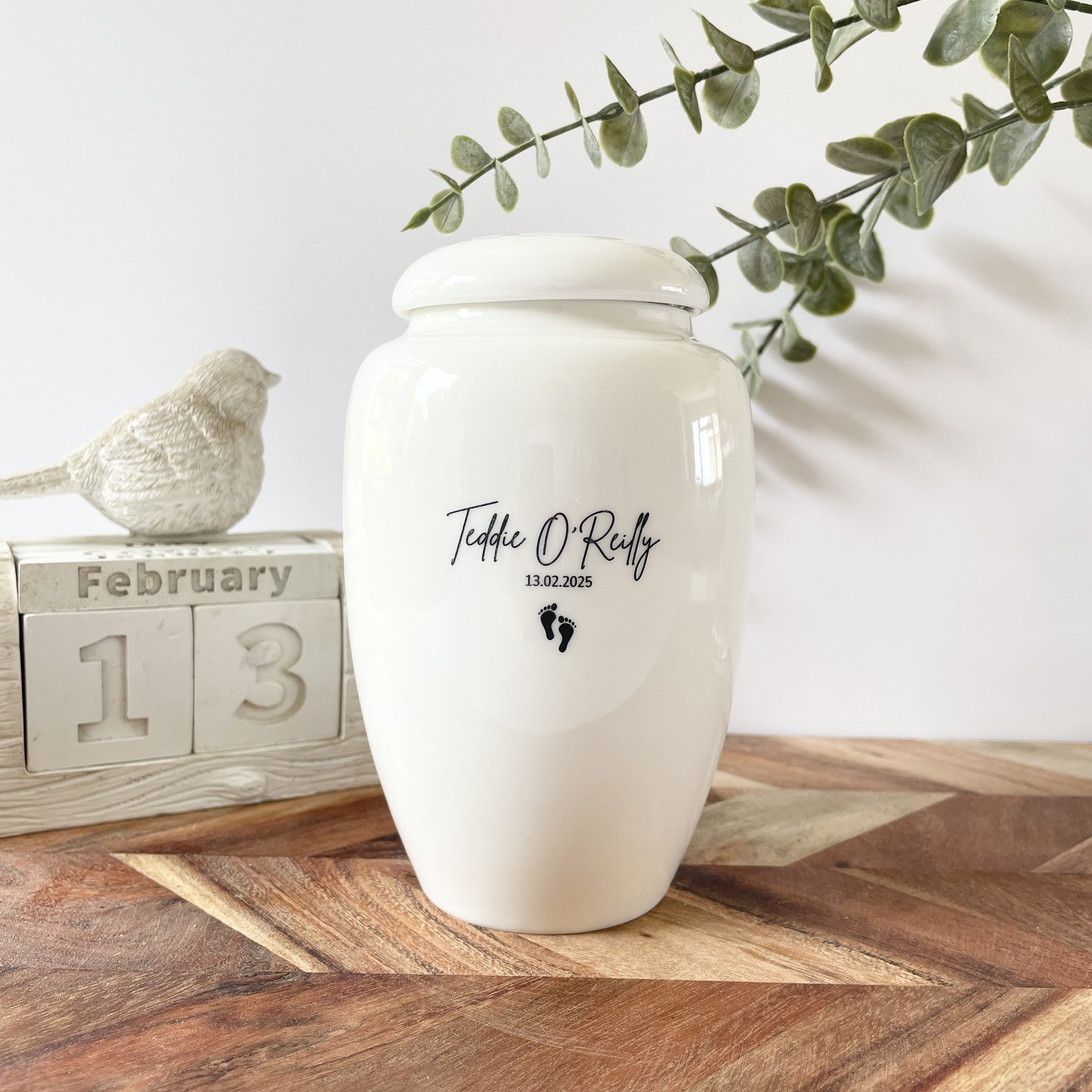 Rounded white ceramic urn with glossy finish, black script text “Monty James Jones” and a small butterfly icon