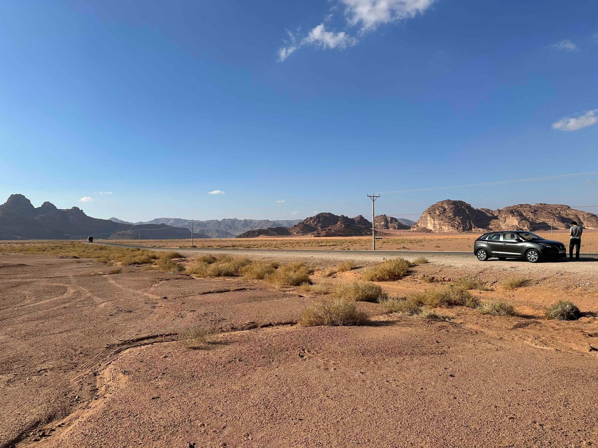 man standing beside white SUV near concrete road under blue sky at daytime