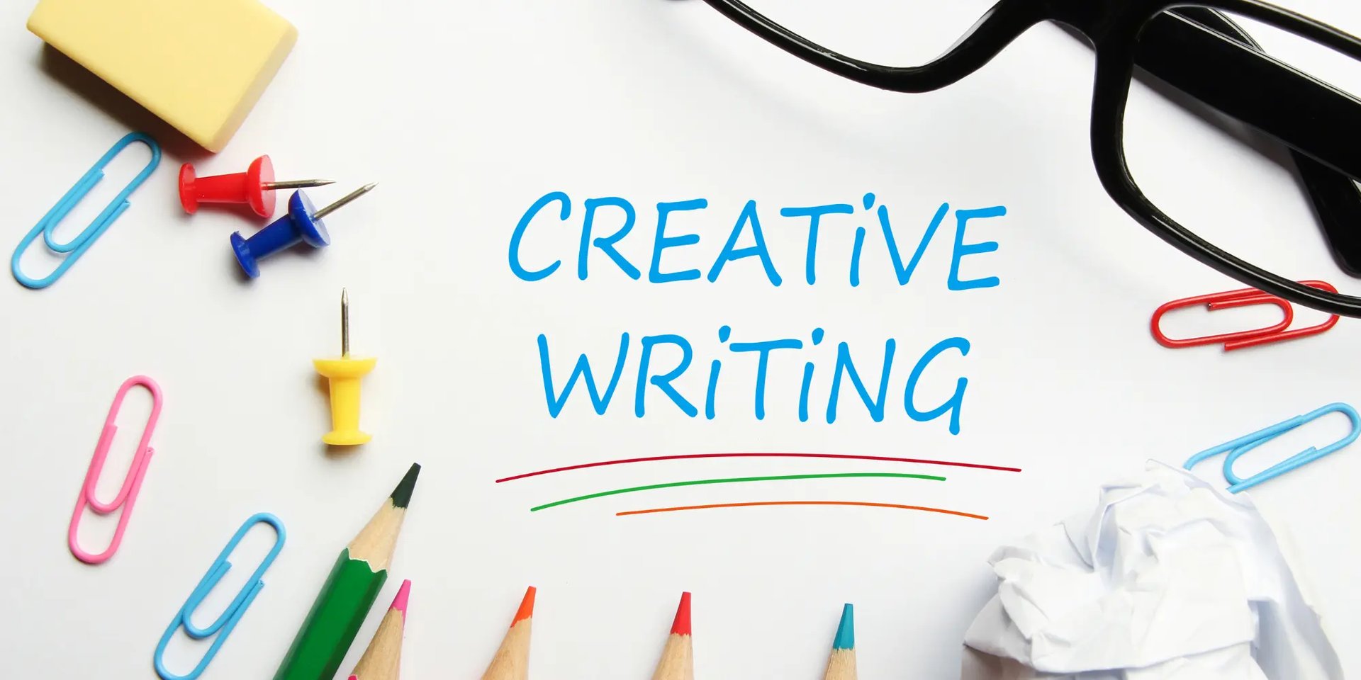 colored pencils, paper pins, paperclips, glasses and a piece of paper with words Creative Writing