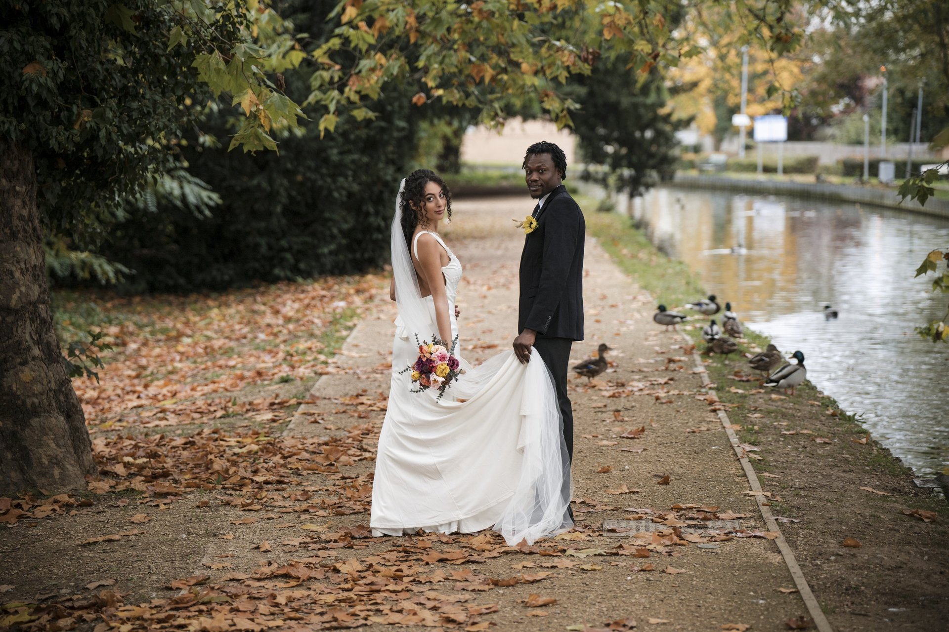 Bride and Groom by a Herts river on their autumnal wedding, with the seasonal leafs having cascaded around them