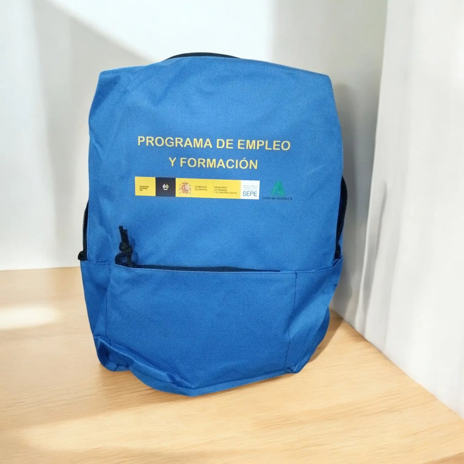 Mochila azul con logotipos del Programa de Empleo y Formación (Gobierno de España, SEPE, Junta de Andalucía)