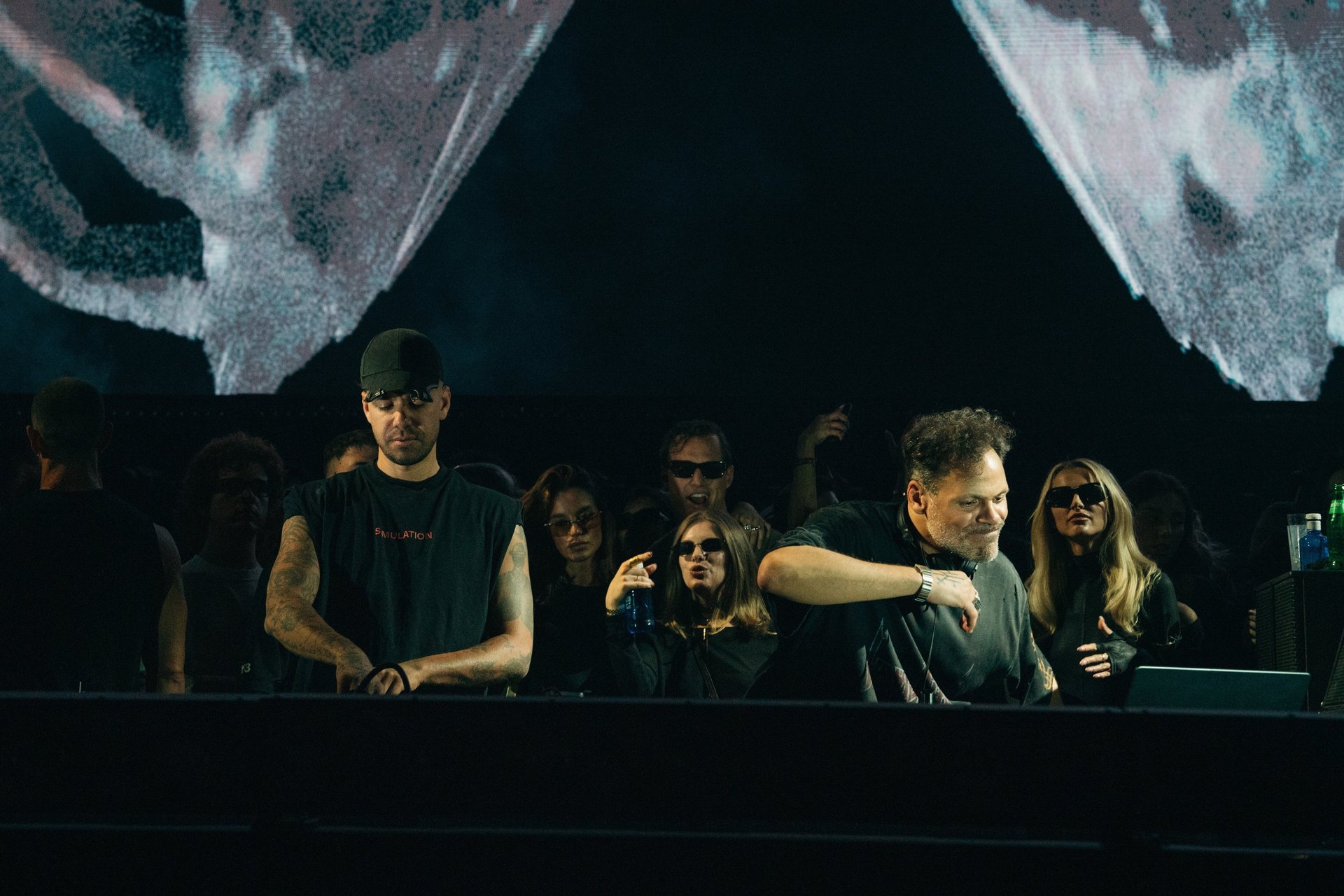 Two DJs performing at Afterlife, Anyma, Tale of Us. Stage lit with visual effects. Concert atmosphere