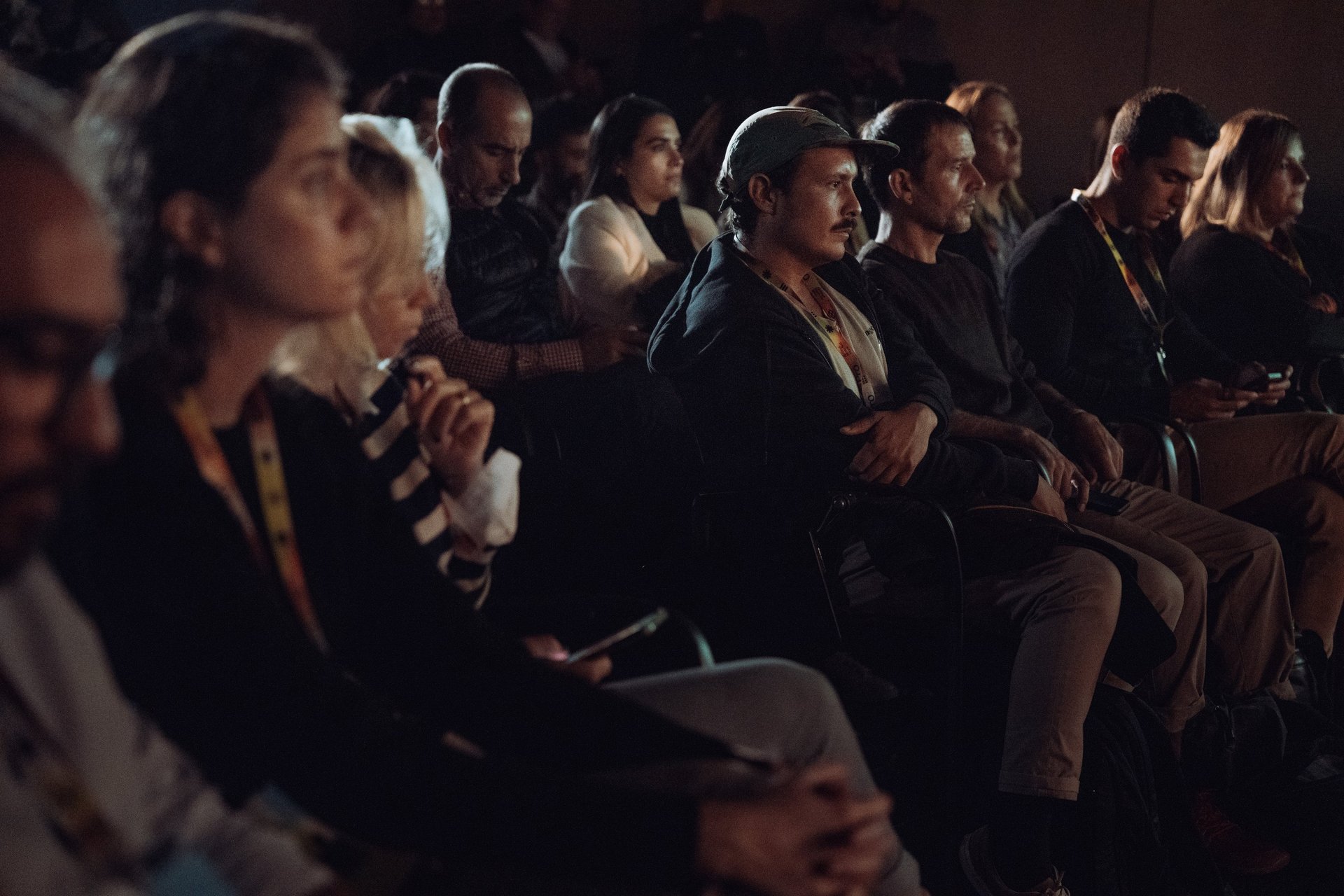 Audience attentively watching a presentation at BIME Bilbao. Various people sitting in rows in a dimly lit room. Conference s