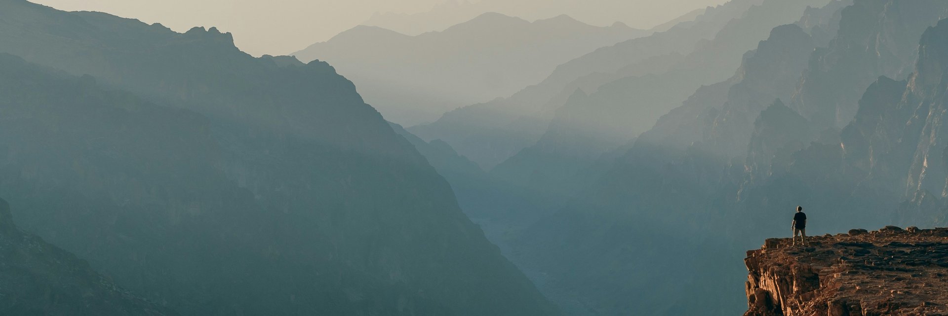 Photo of hiker on a cliff, looking out at the mountain range