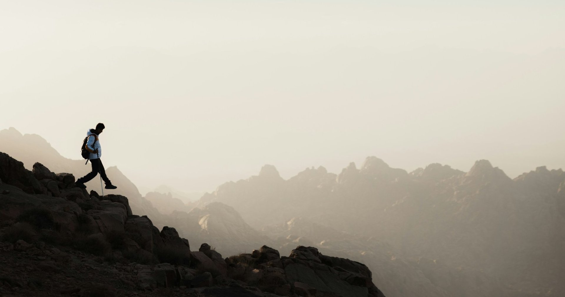 A man hiking on a rocky mountain, with a hazy mountain range in the background