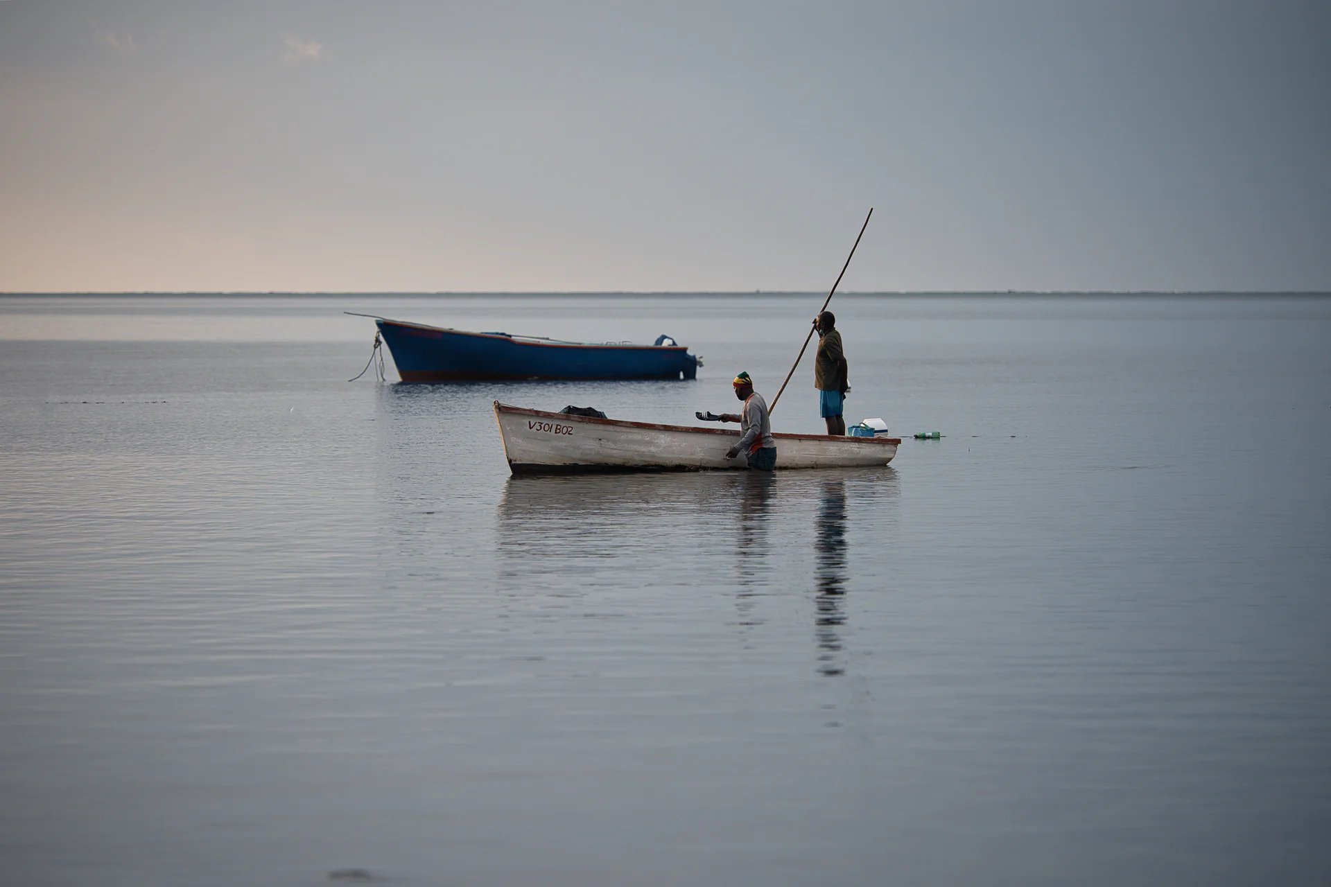 Fishermen at Petite Case Noyale on a traditional wooden boat in calm waters of Mauritius, reflecting the serene early morning