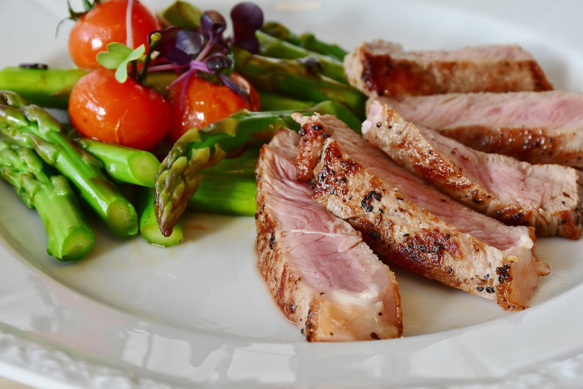 een bord met daarop groene asperges , tomaten en een stukje mals vlees