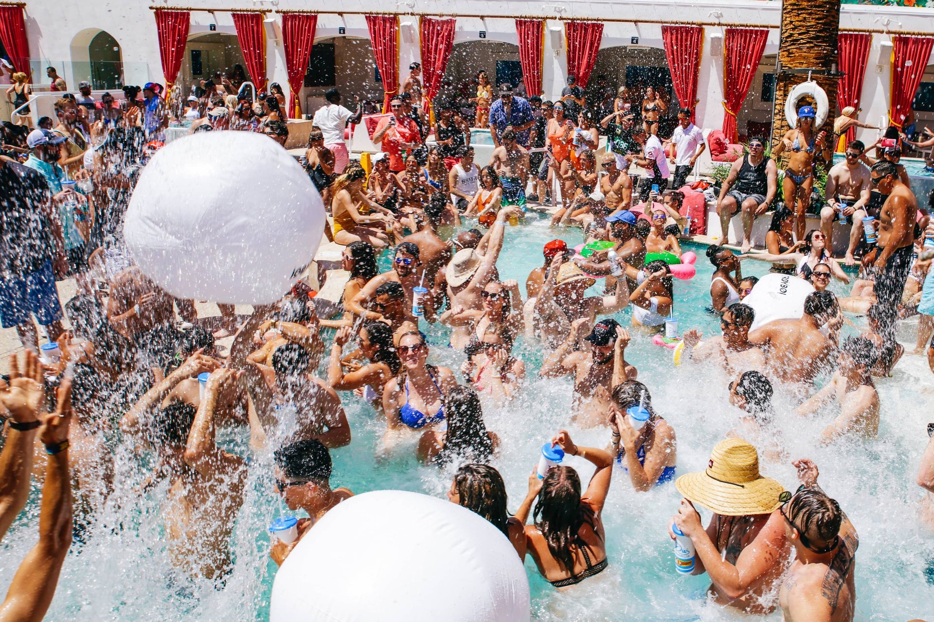 Crowd enjoying a lively pool party at a Las Vegas dayclub with water splashing, inflatable toys, and drinks.