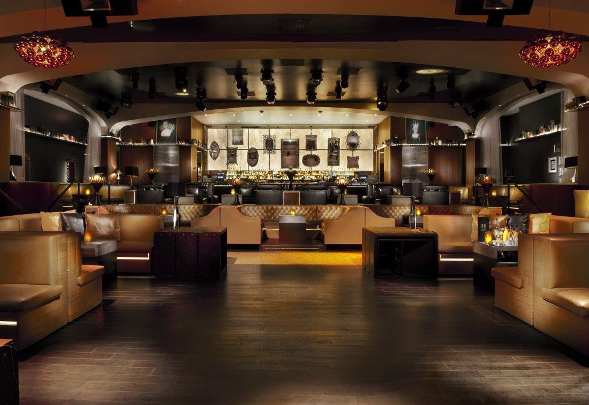 Elegant nightclub interior featuring modern decor with leather seating, a well-lit bar, and dark wooden floors.