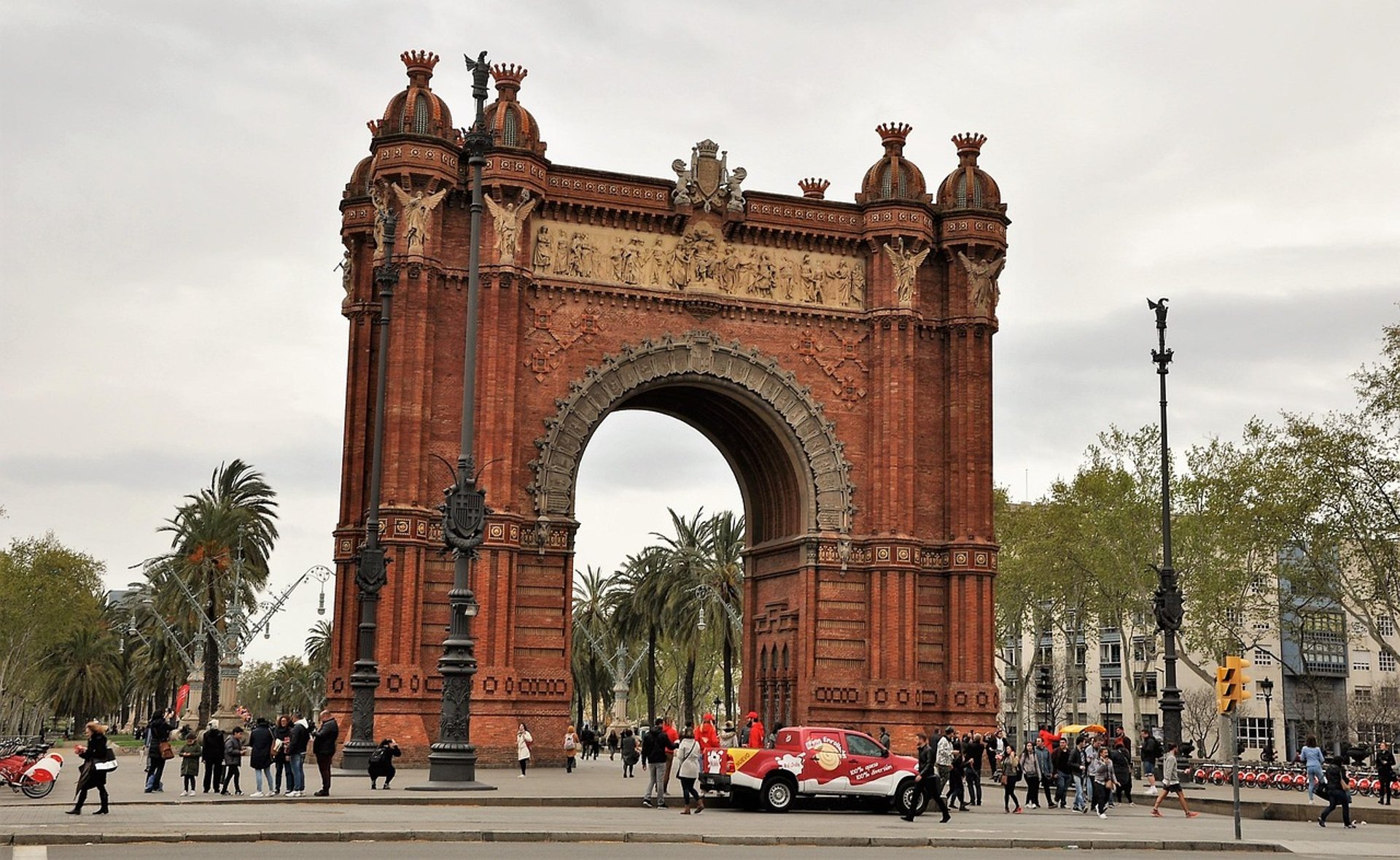 Arc de Triomf in Barcelona—red-brick triumphal arch leading to a palm-lined promenade, with pedestrians and a small vehicle