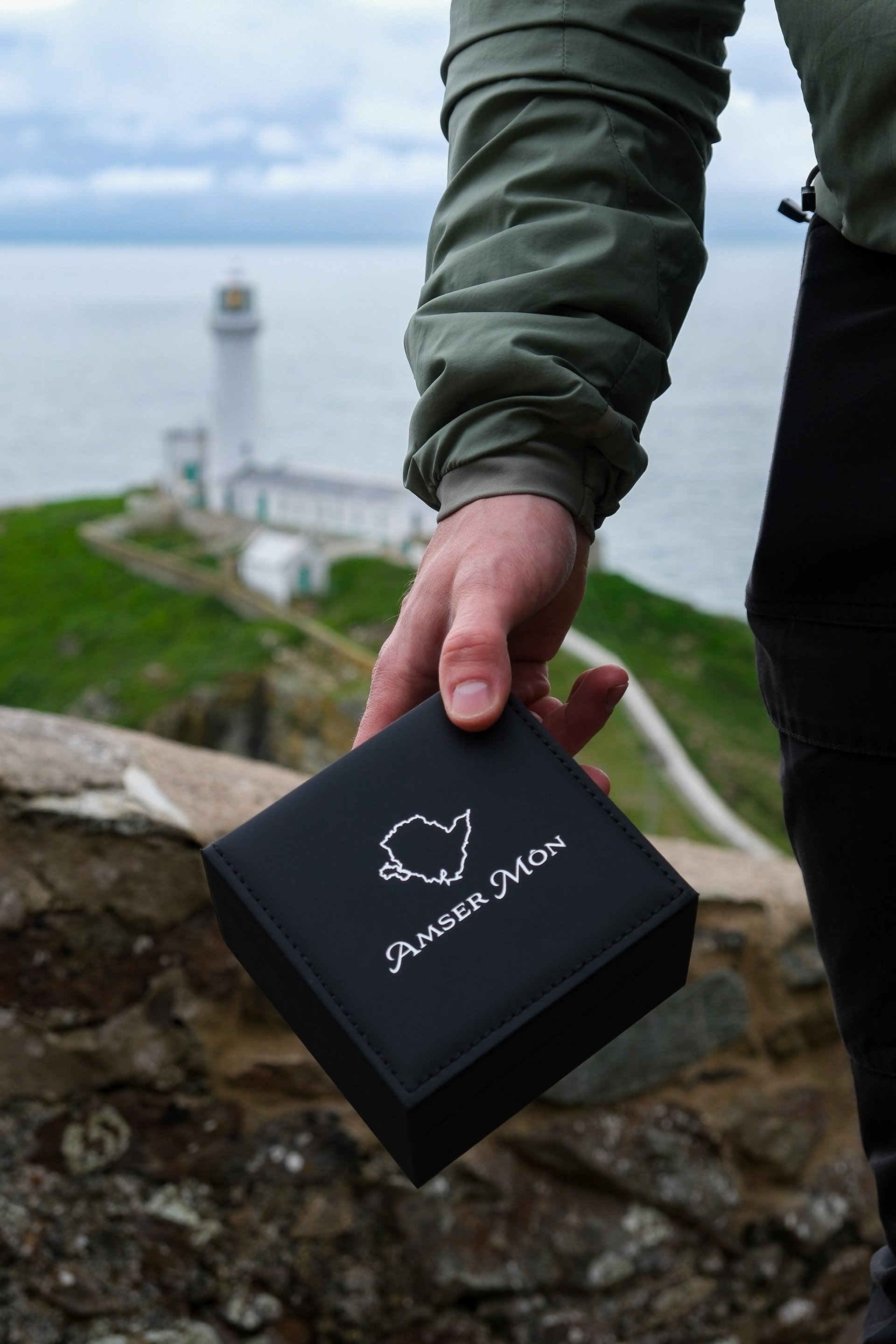 Amser Mon Anglesey branded box being held next to South Stack, Anglesey, Wales