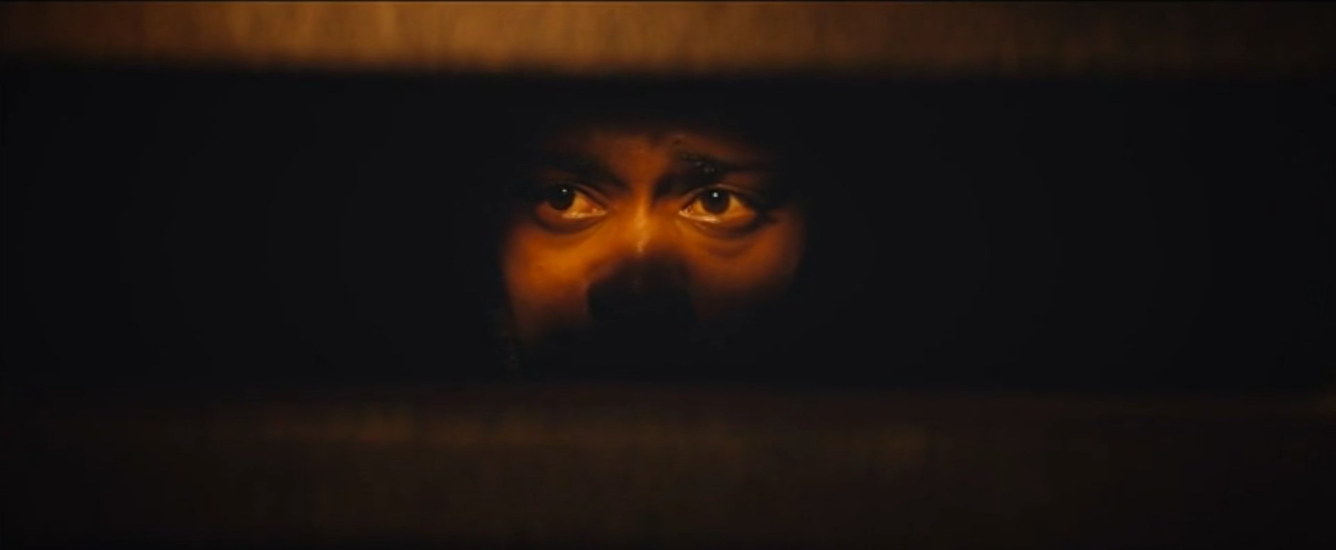 Screenshot from the 2018 film Sorry to Bother You showing a close up of a face in shadow apart from his eyes.