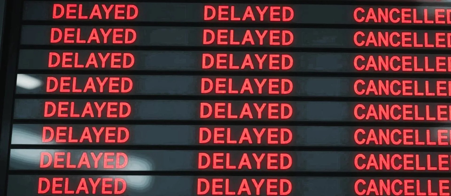 Airport flight information board with multiple rows showing flight status as Delayed and Cancelled in red text.