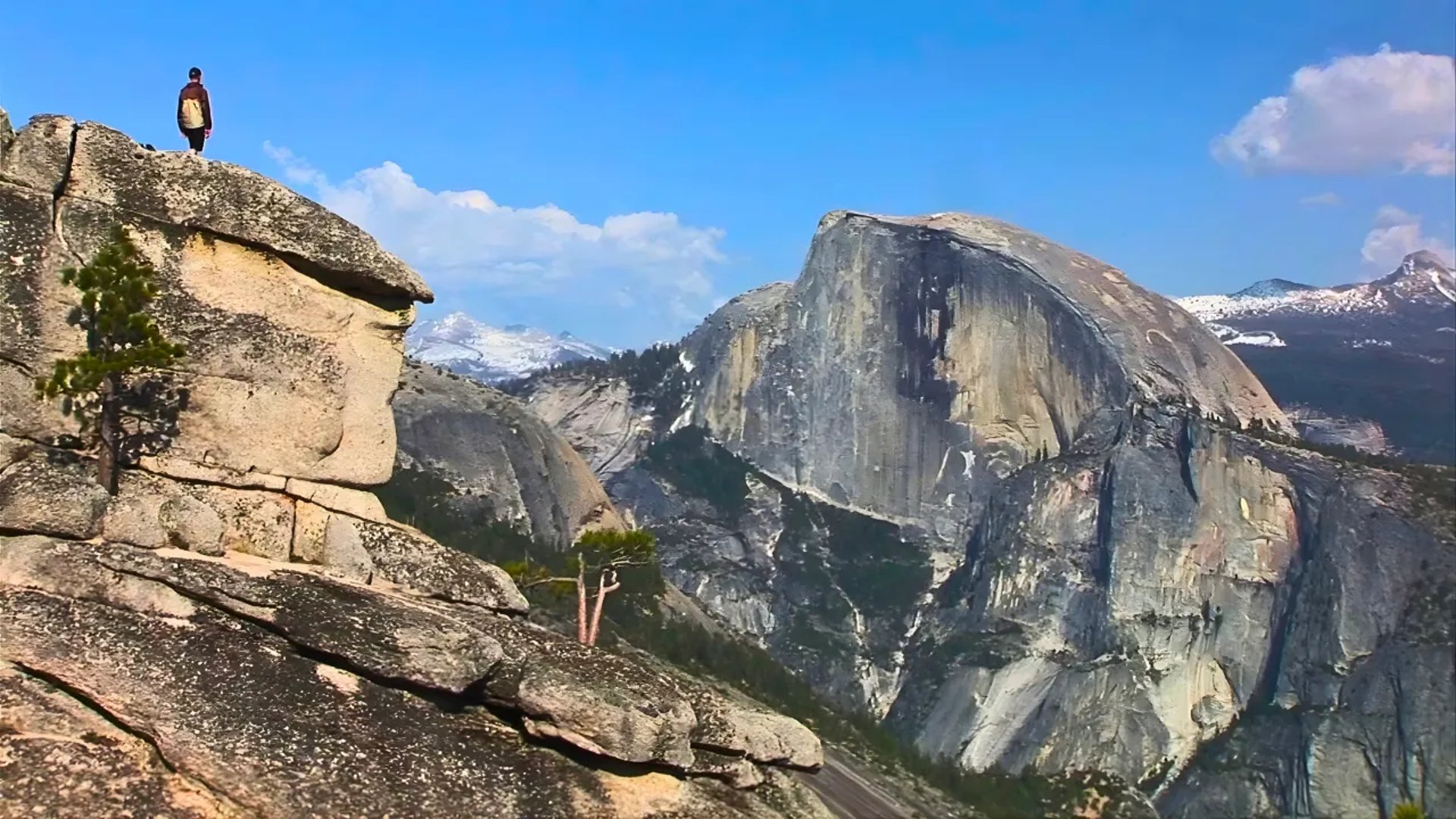 Hiker on a rocky cliff overlooking the iconic Half Dome in Yosemite National Park.