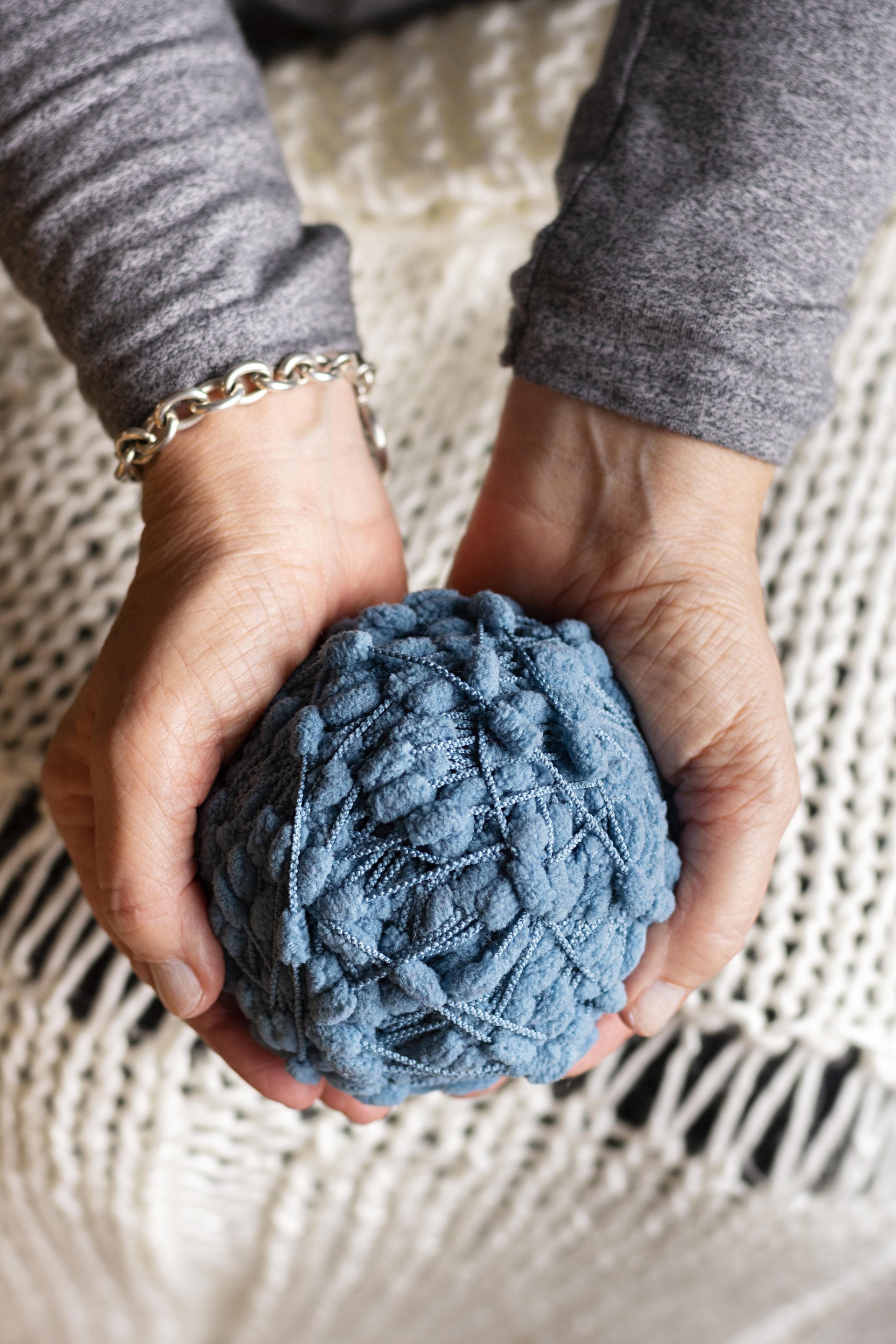 unas manos sujetando amorosamente una bola de estambre azul 