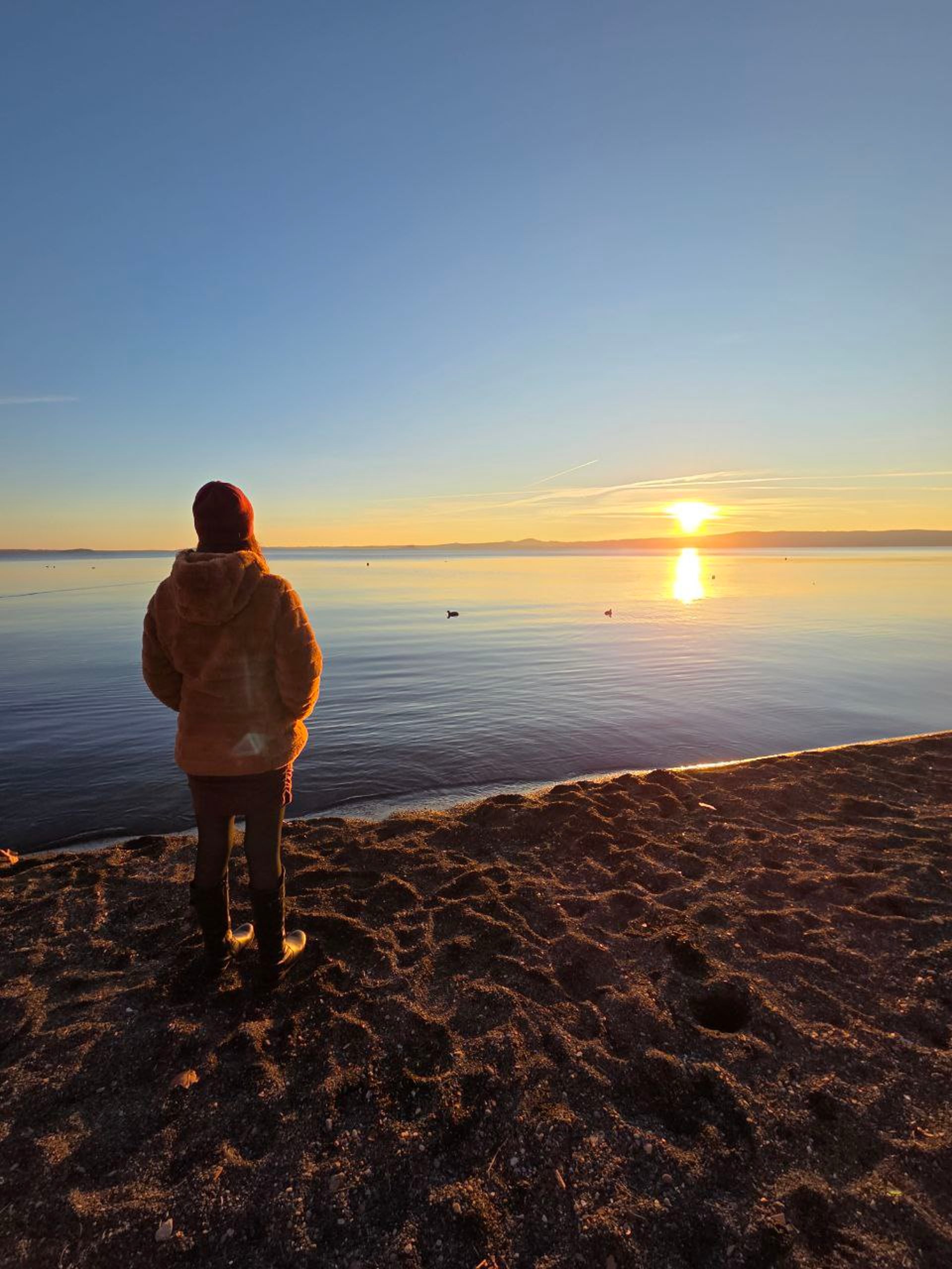 Donna che guarda l'orizzonte, sulla spiaggia con il mare di fronte al tramonto