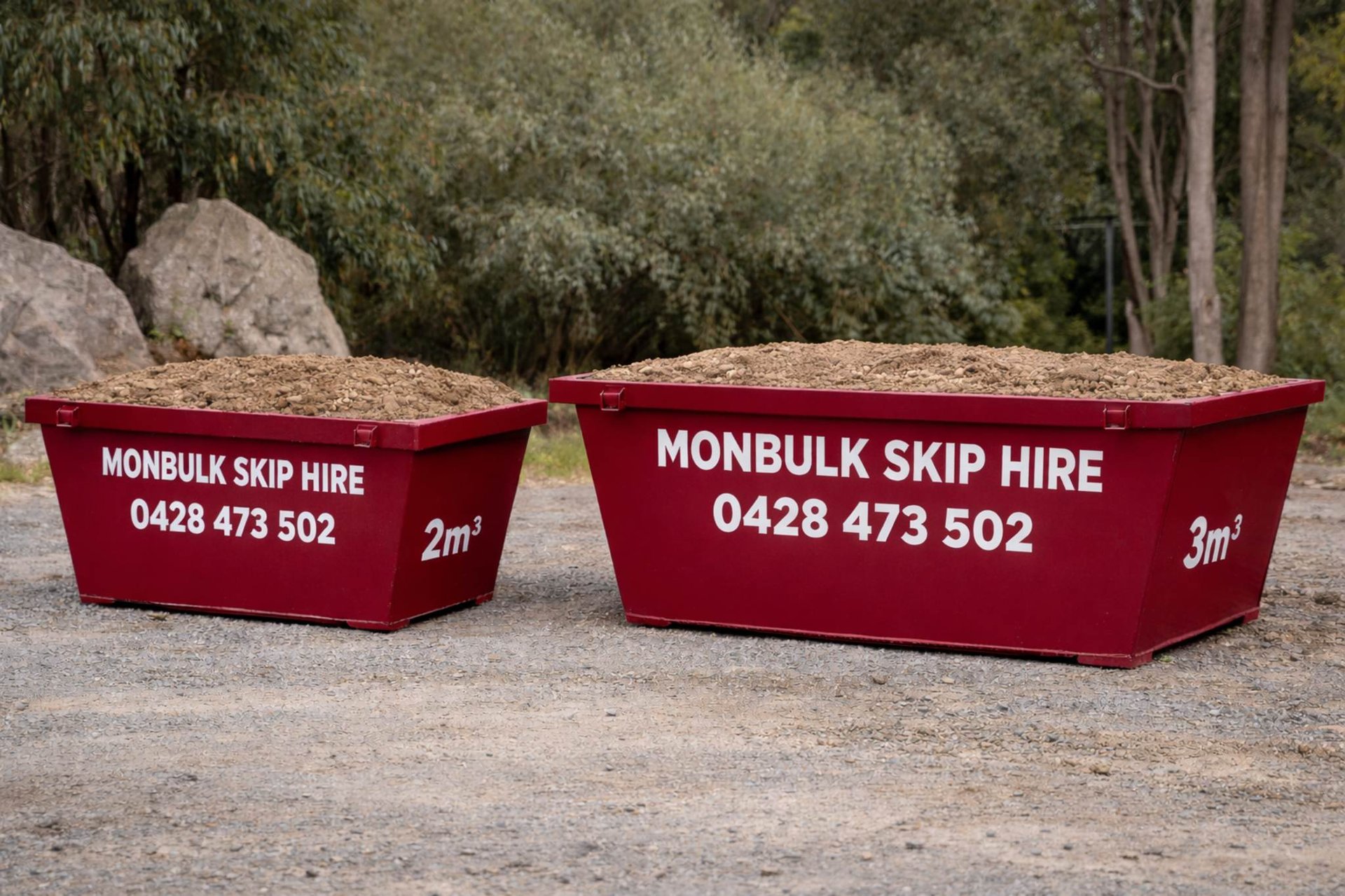 2m3 and 3m3 maroon skip bins resting on a gravel surface filled with soil, dirt, clay