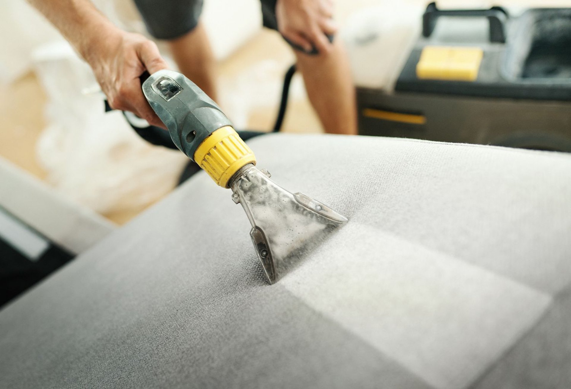a woman in a green shirt and black gloves vacuuming a gray ottoman