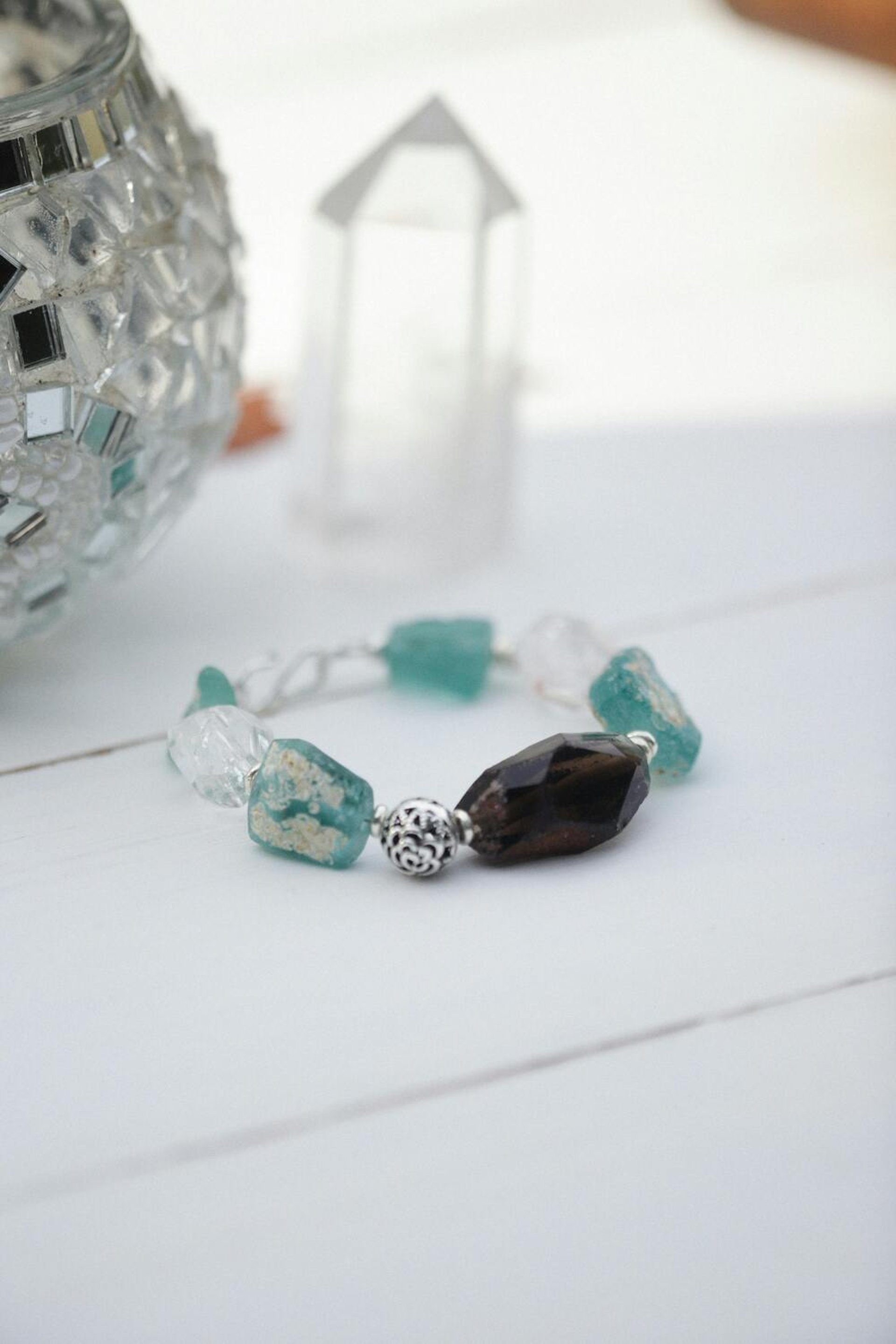 Pulsera de cuentas hecha a mano con cristal marino turquesa y cuarzo ahumado sobre una superficie blanca.