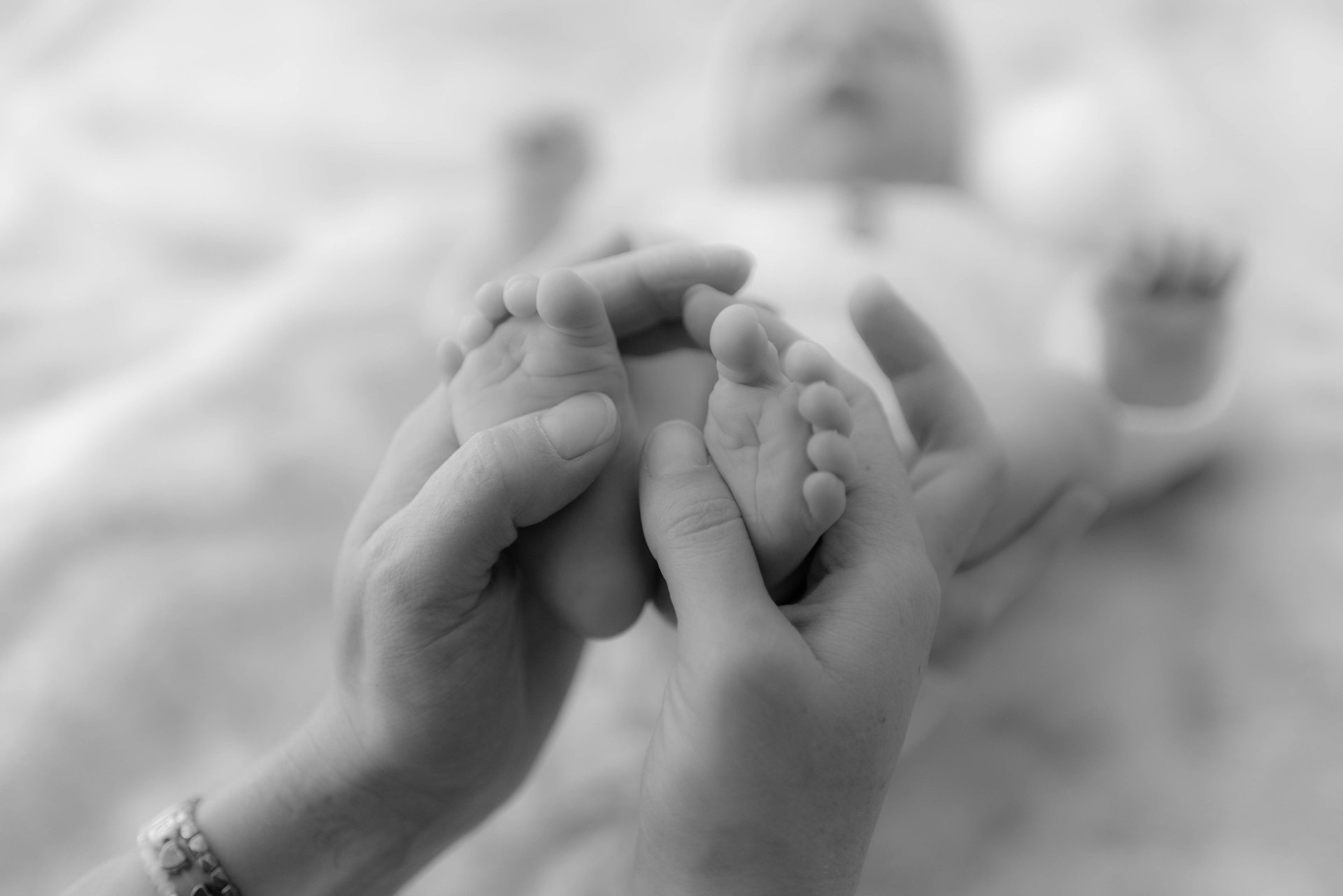 Photo en noir et blanc des pieds de bébé entourés de mains réconfortantes