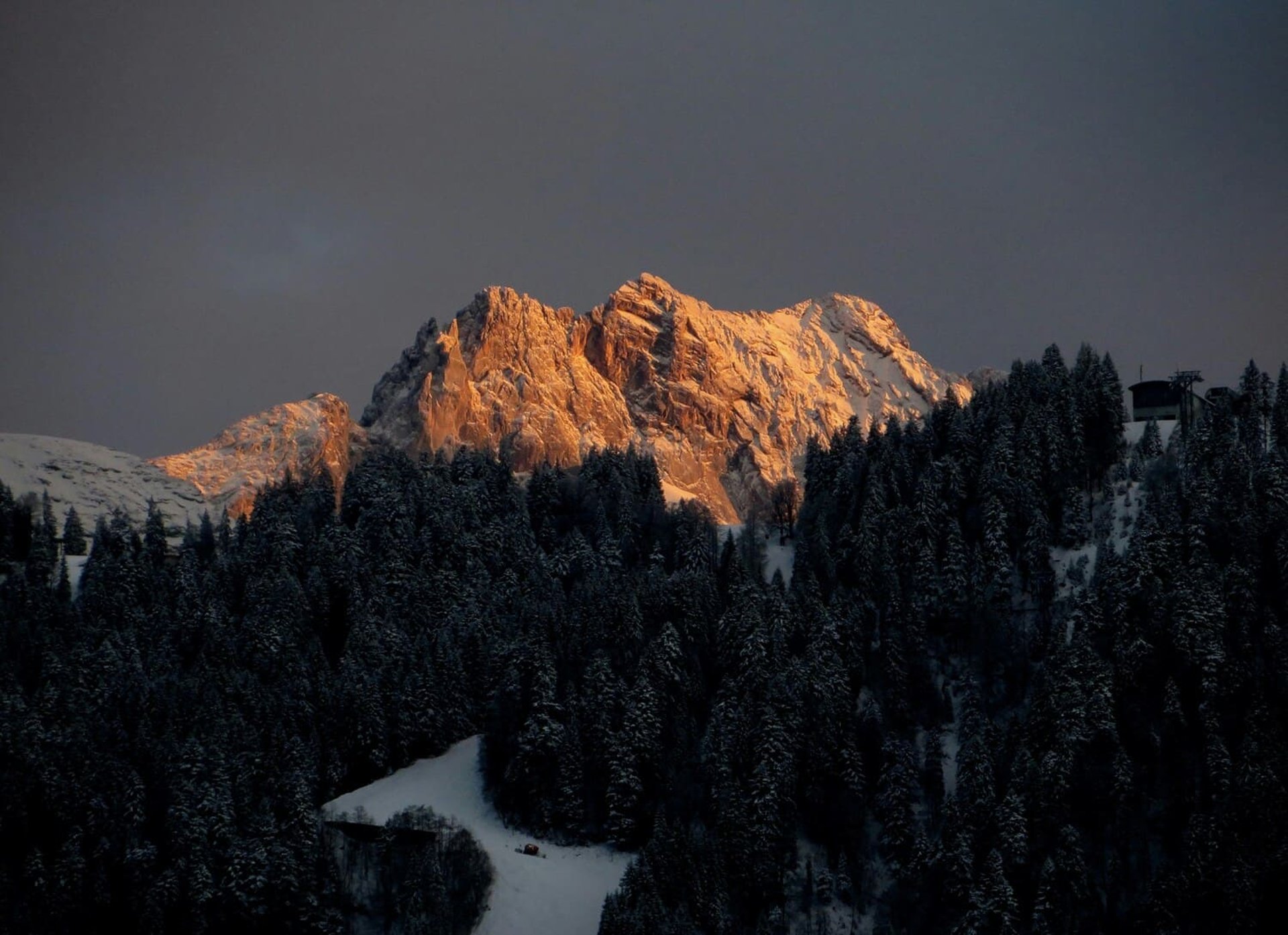 Paisaje de montaña iluminada por el sol, con nieve y pinos.