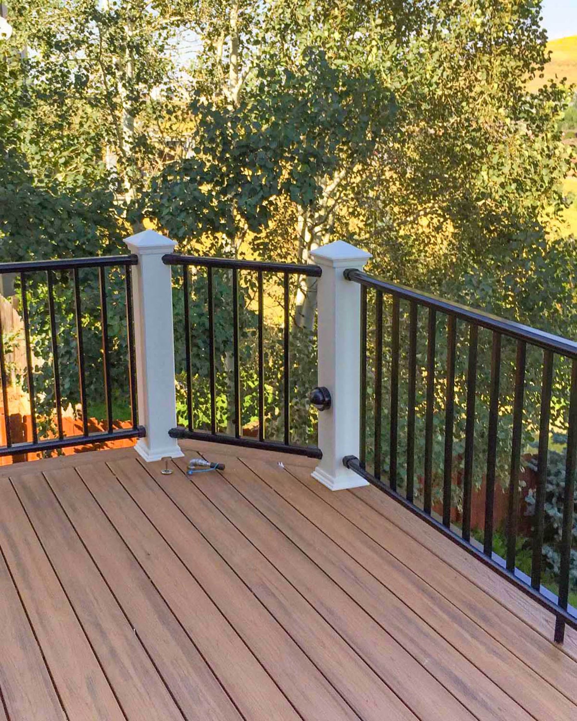 Close-up of a completed composite deck corner with white posts, black aluminum balusters, and mountain views.