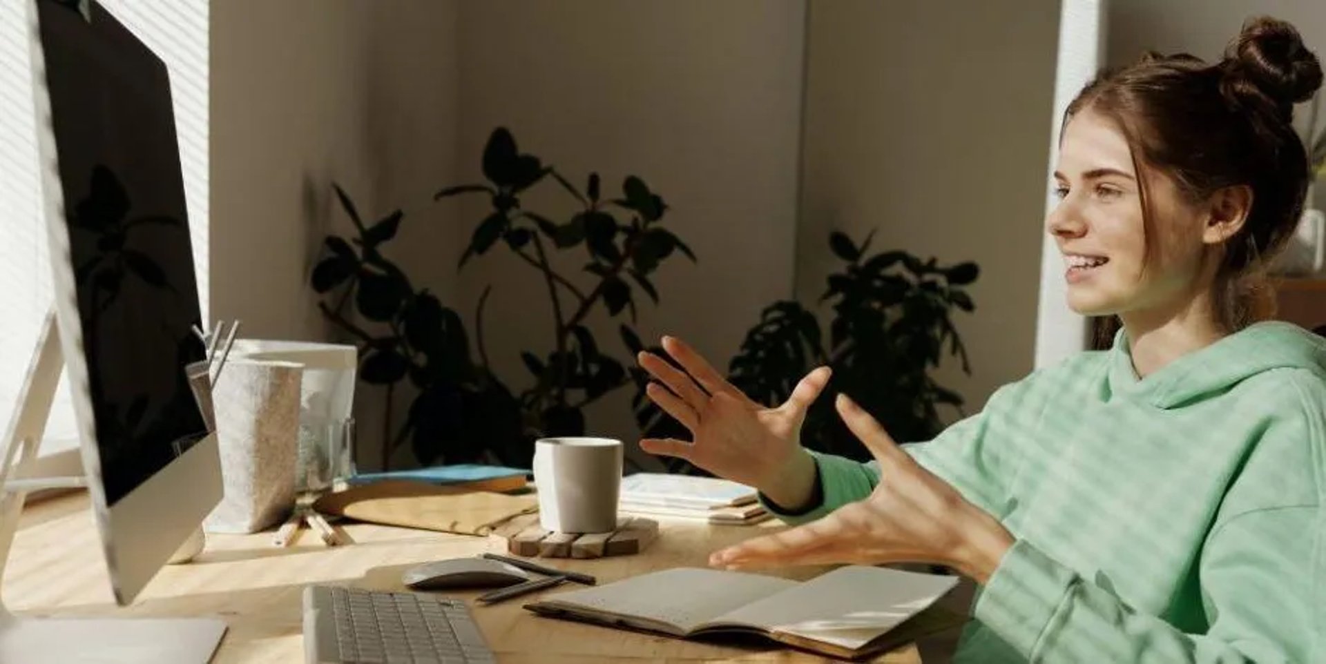 Femme en visio à son bureau, parlant devant un écran avec des gestes des mains